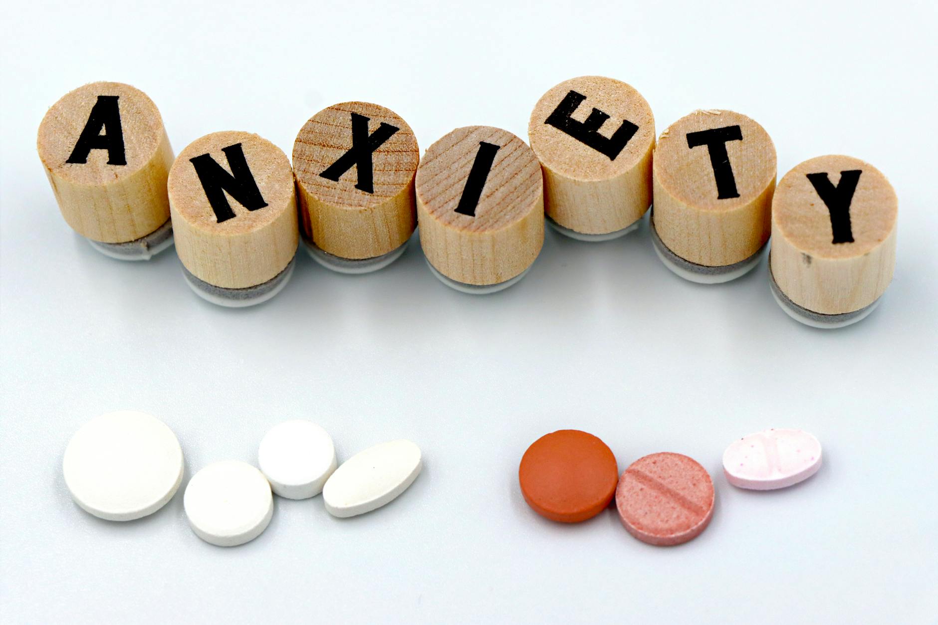 Wooden blocks spelling 'Anxiety' with assorted pills below on a light background. - types of anxiety disorders