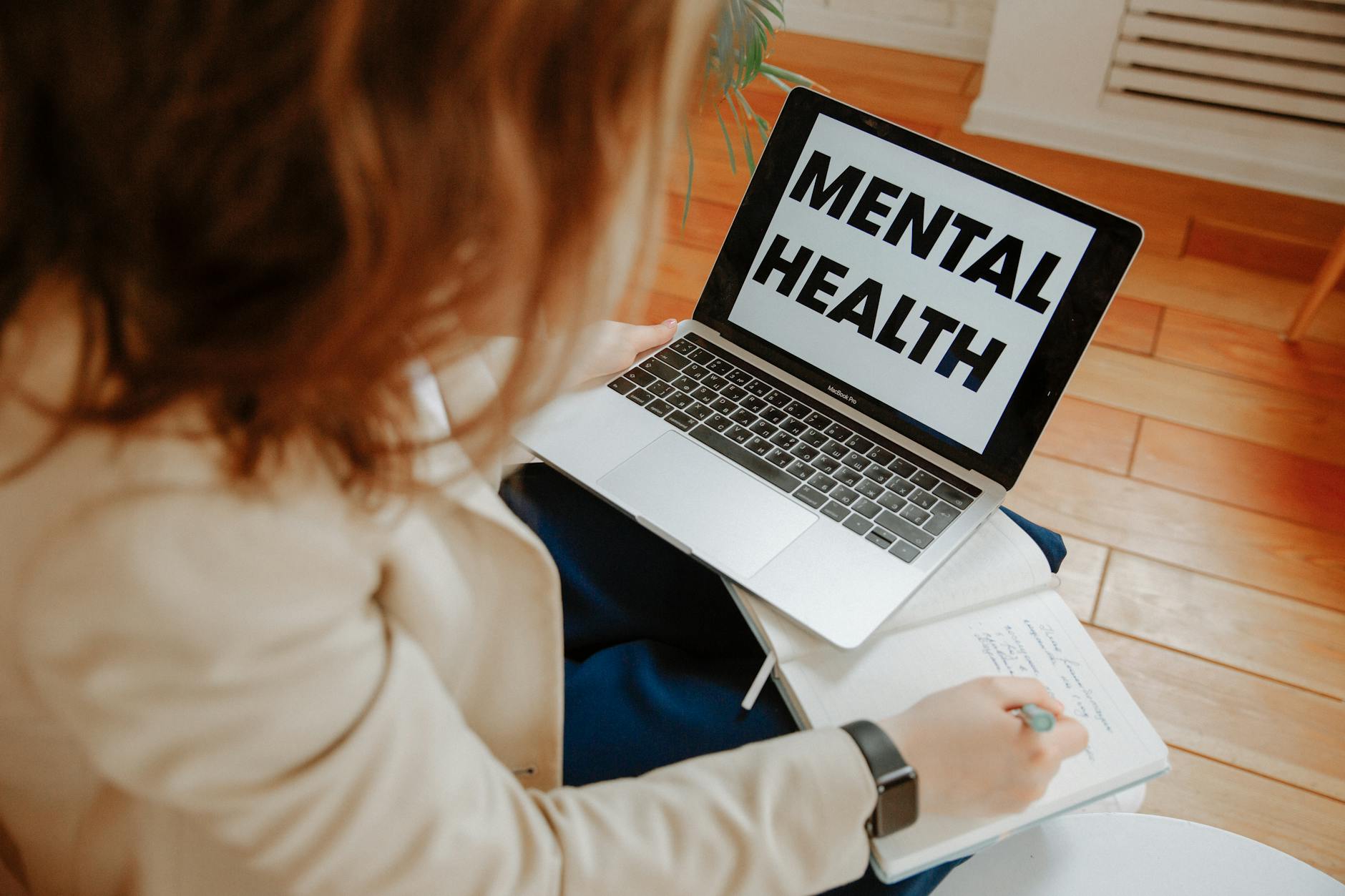A woman participating in an online therapy session, taking notes with a laptop displaying 'Mental Health'. - virtual therapy benefits