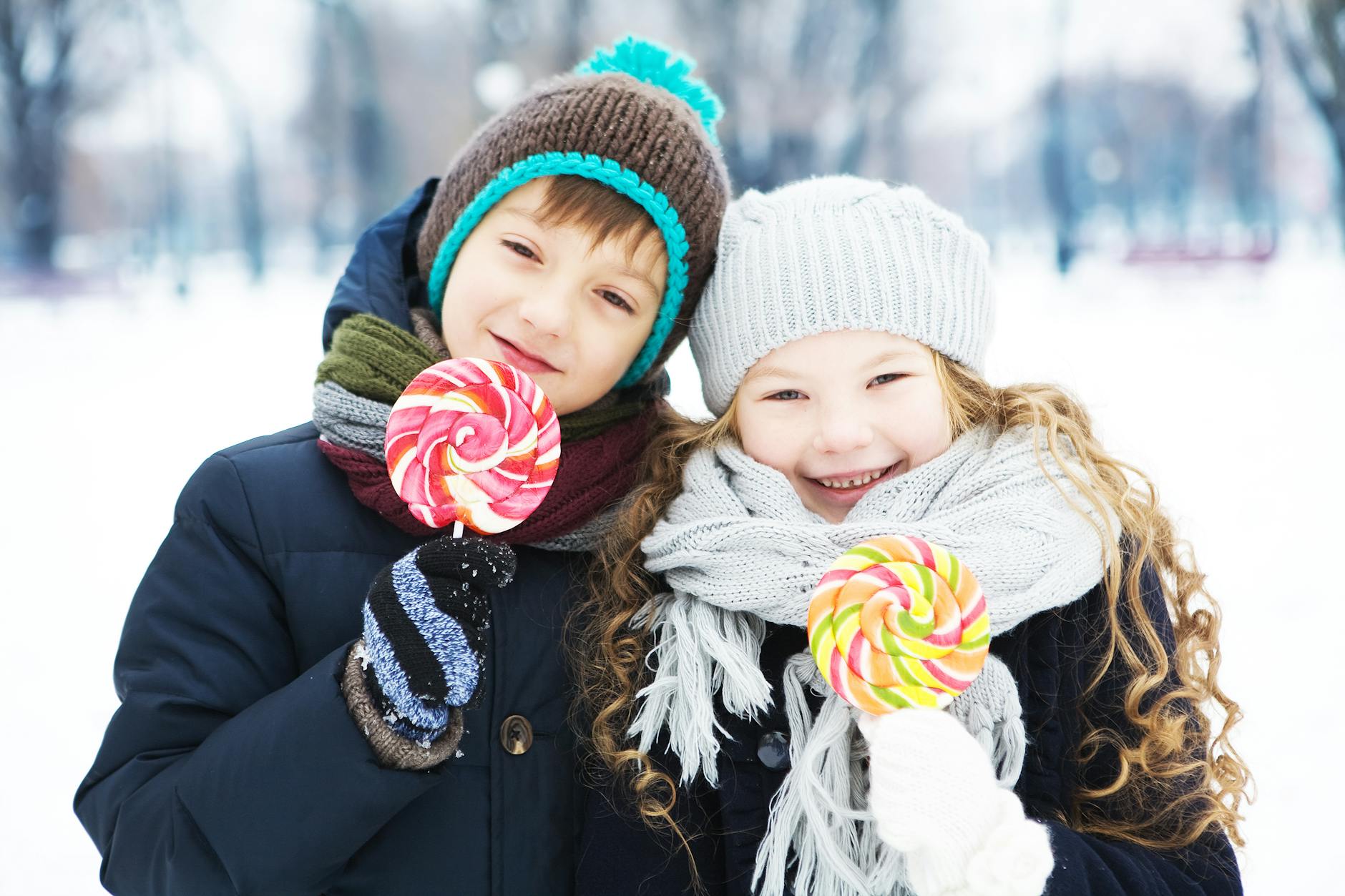 Two children happily enjoy lollipops in winter wear, smiling in a snowy outdoor setting. - winter anxiety children
