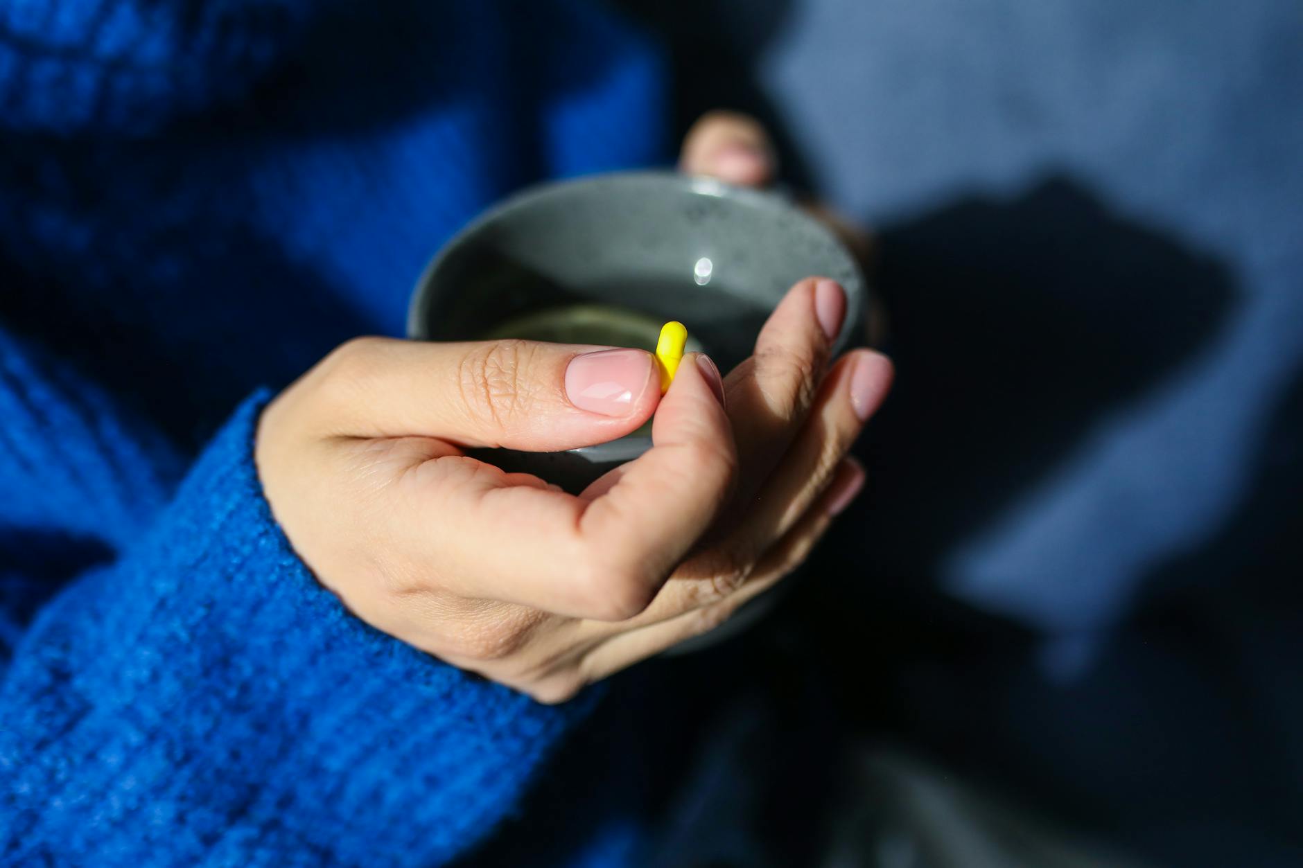 Close-up of hands holding a hot drink and yellow pill, indicating health and wellness theme. - winter blues treatment