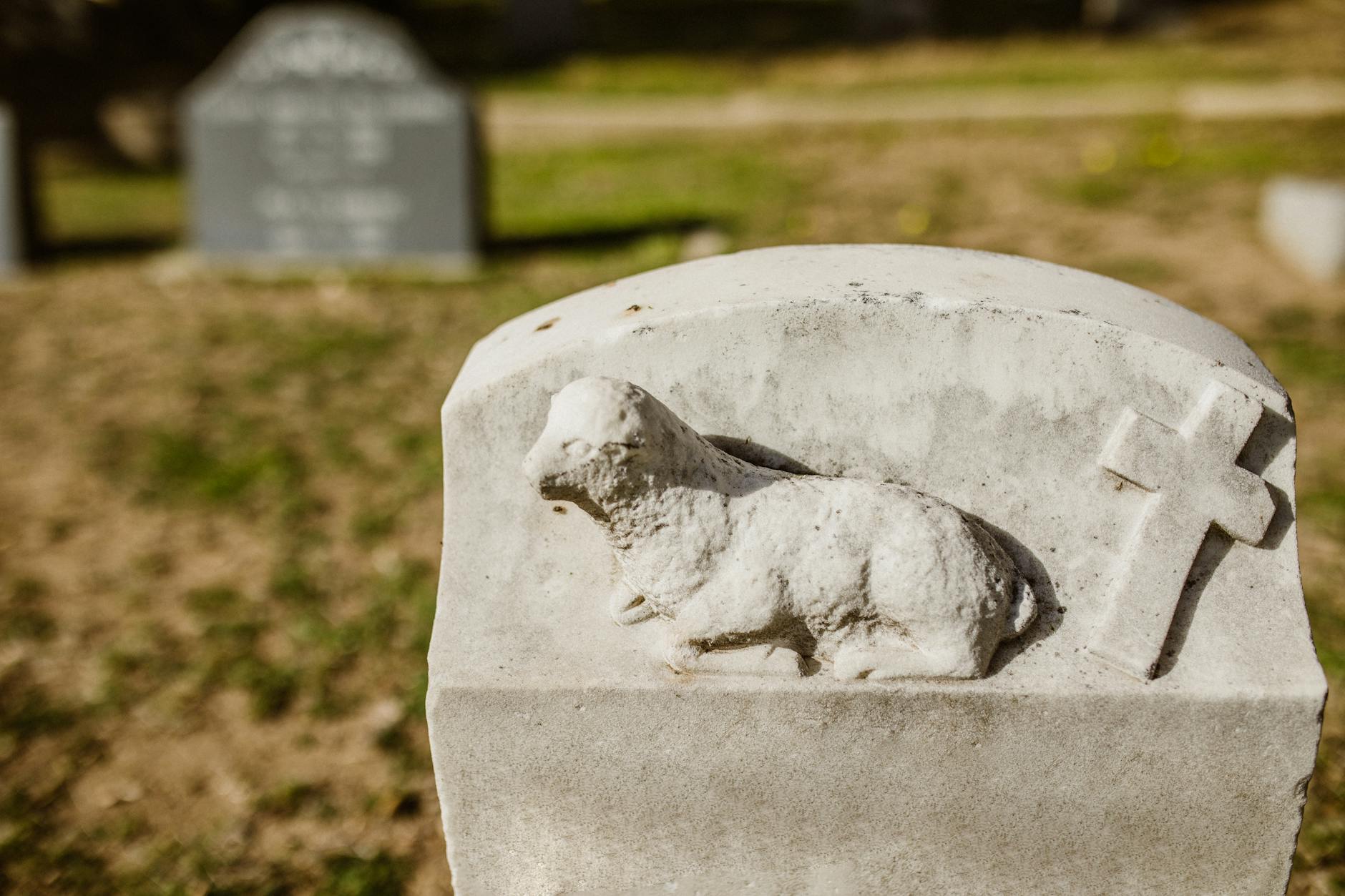 Detailed view of a lamb sculpture and cross on a tombstone in a serene cemetery setting. - winter grief therapy