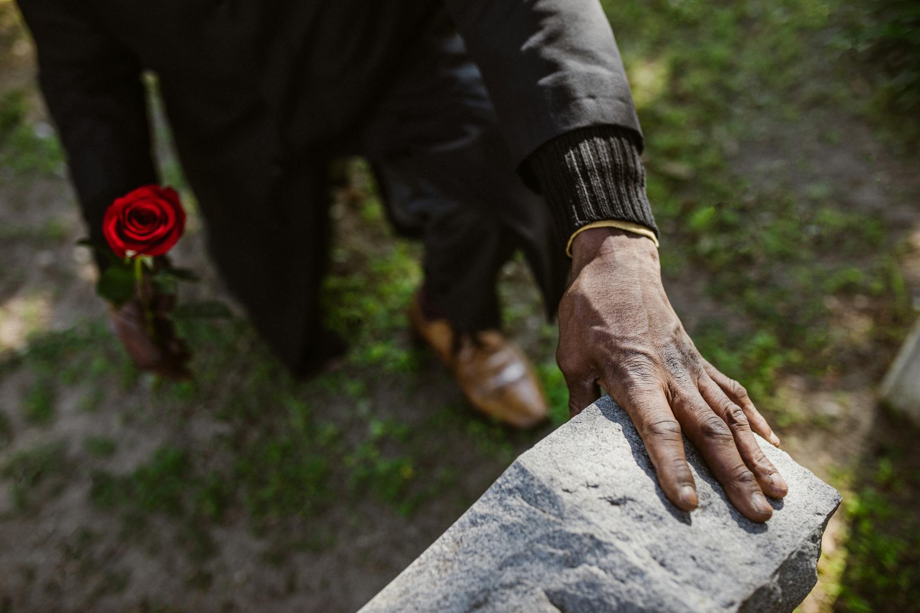 A man mourns a loved one, holding a rose by a gravestone, signifying loss and remembrance. - winter grief therapy