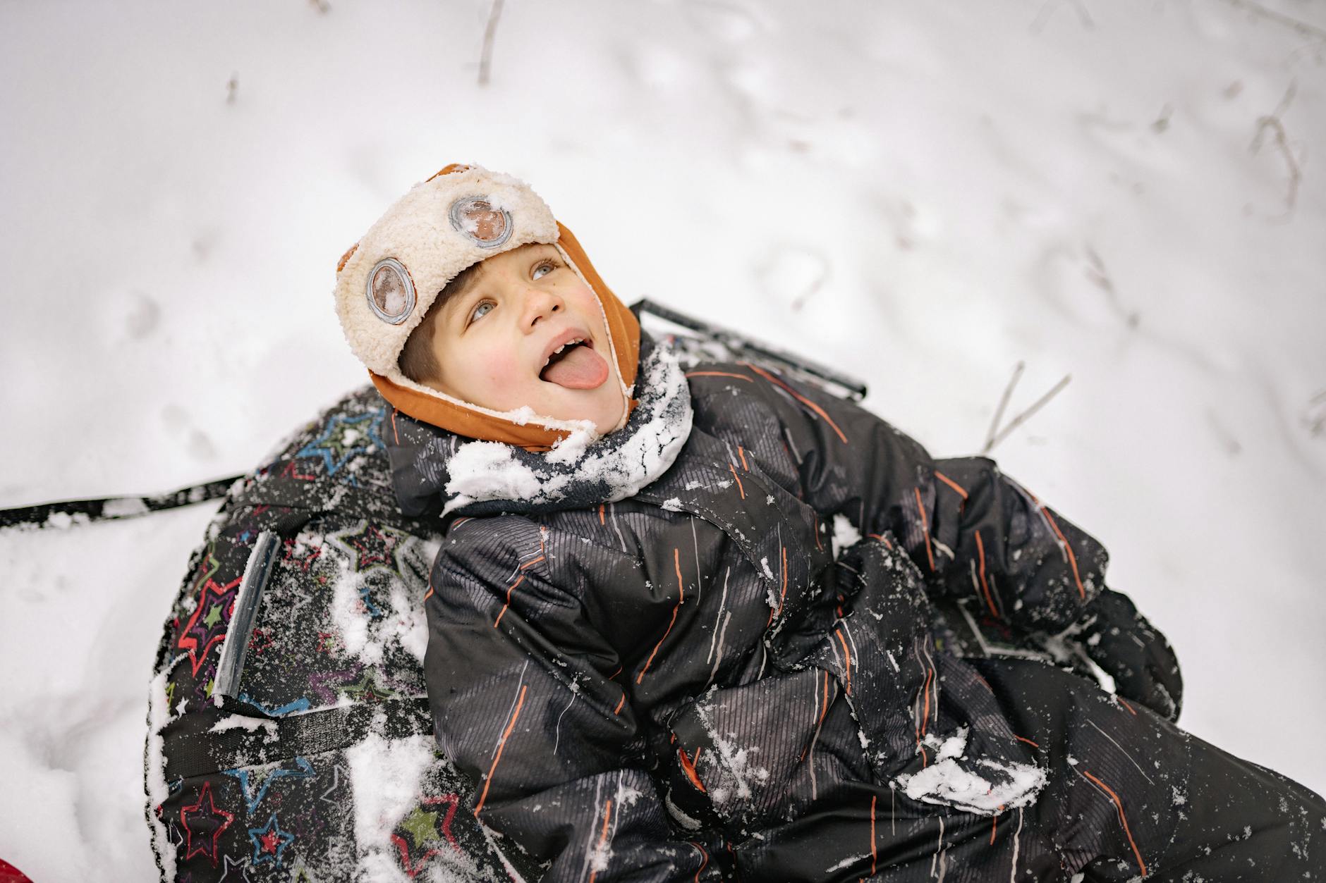 A child in winter clothing enjoying the snow with a big smile and playful spirit. - winter kids activities