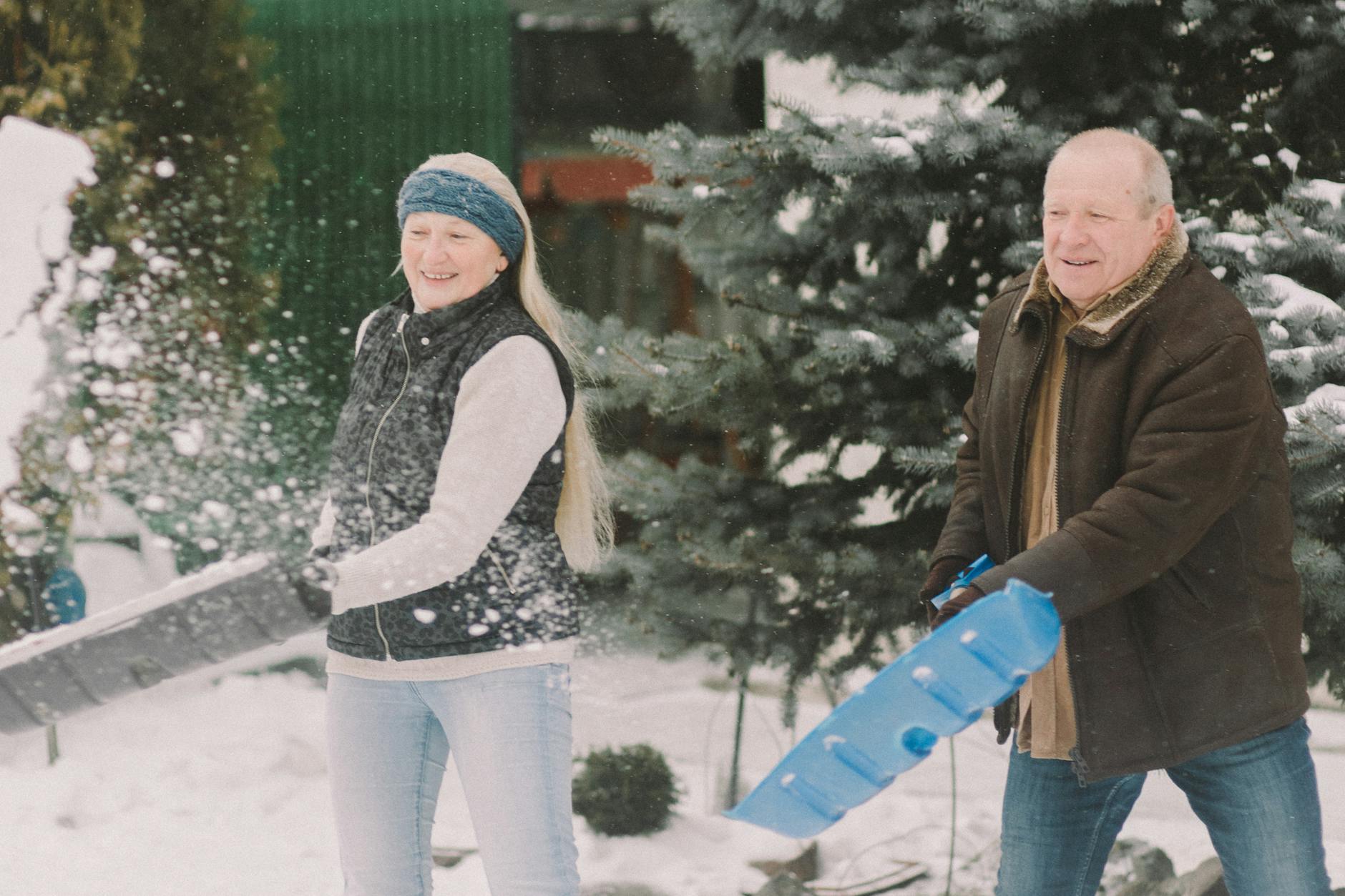 An elderly couple happily shovels snow together outdoors, embracing the winter season. - winter marriage blues