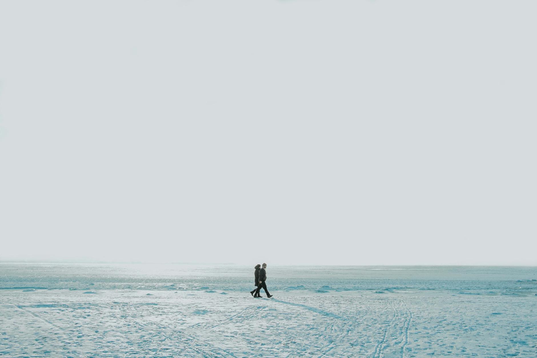 Two individuals walking on a vast snowy landscape under a clear sky, exemplifying solitude and winter serenity. - winter marriage blues