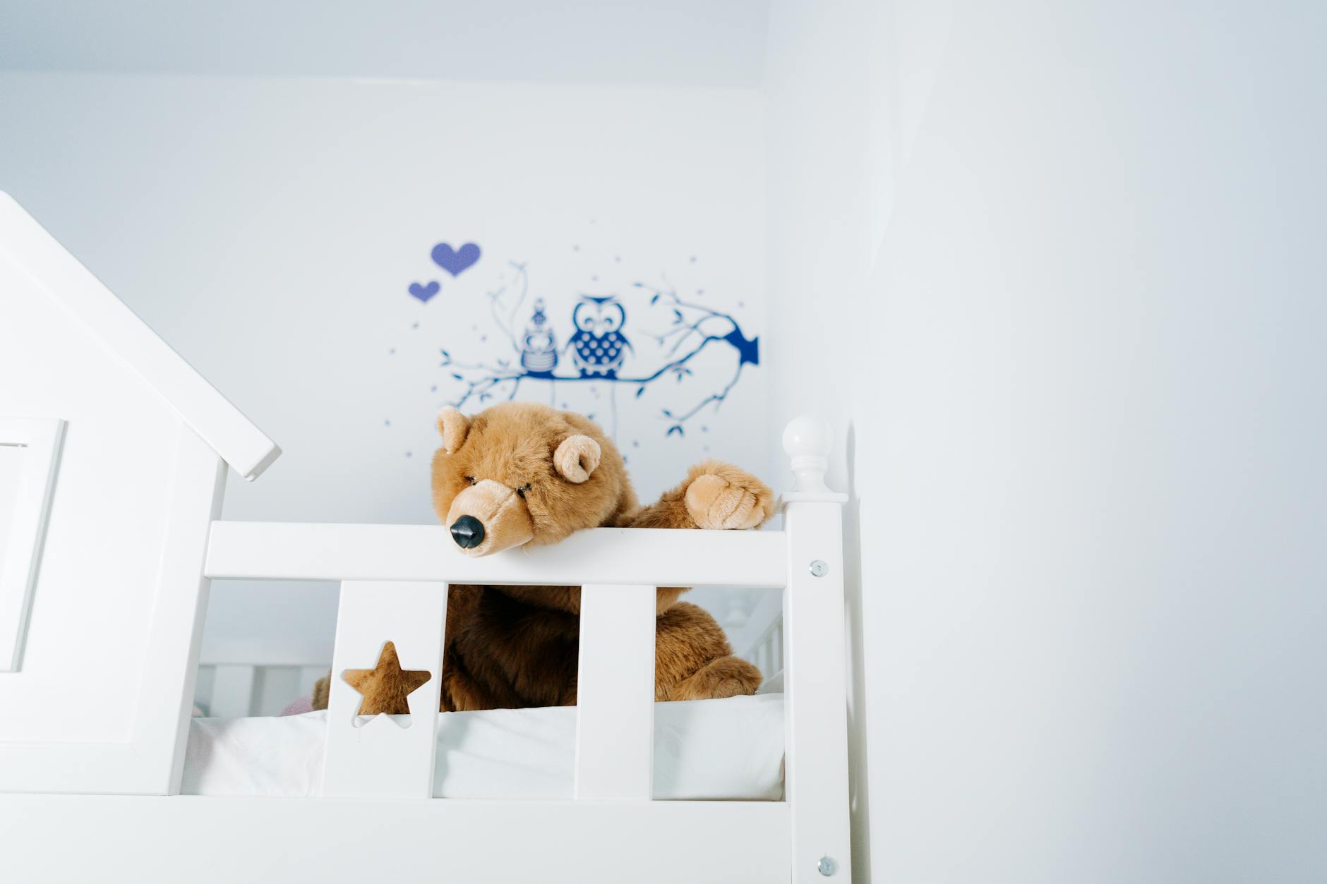 A plush teddy bear rests on a child's bed with charming owl-themed wall art. - winter sleep children