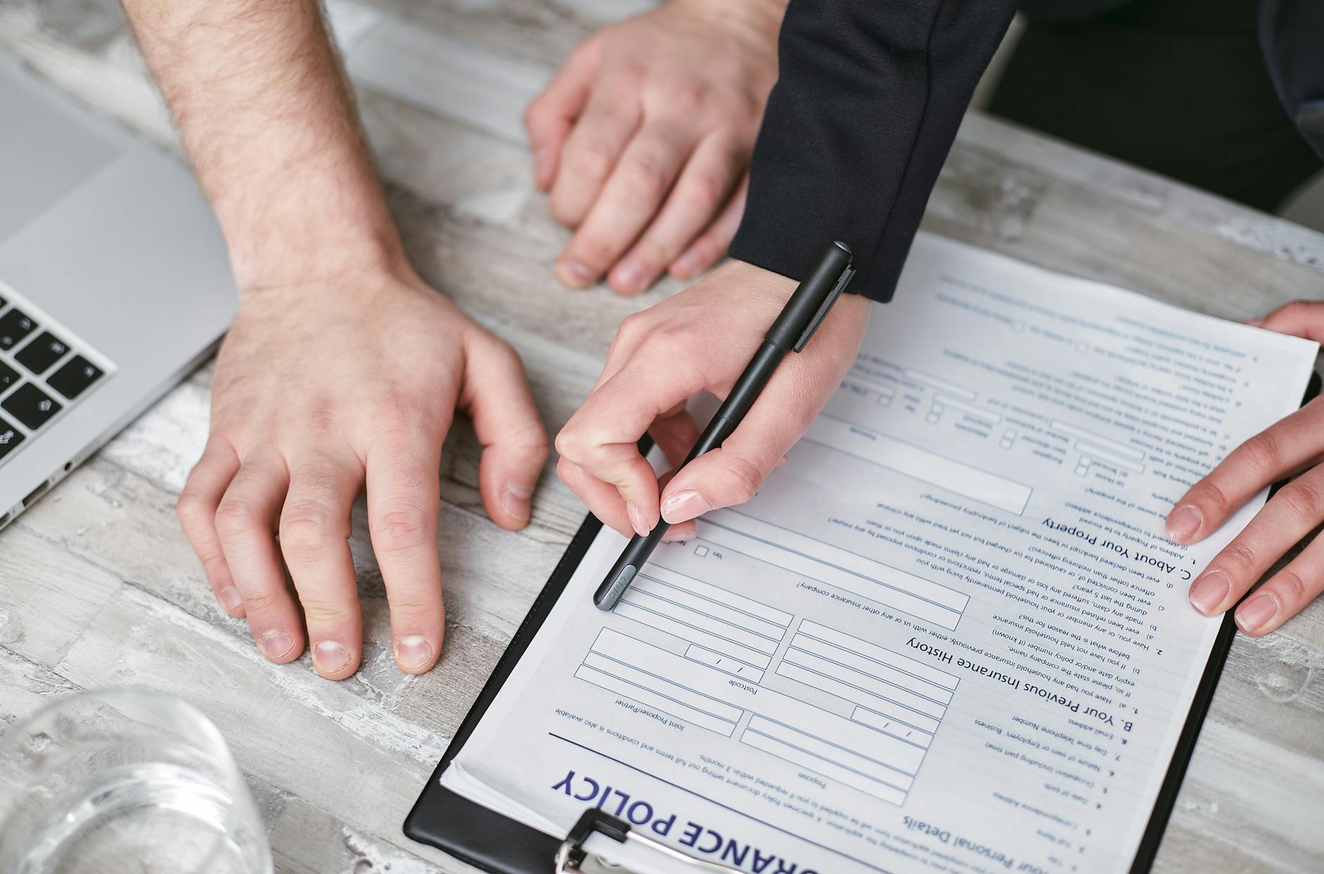 Close-up image of two people signing an insurance policy document on a wooden desk. - workplace dating policy