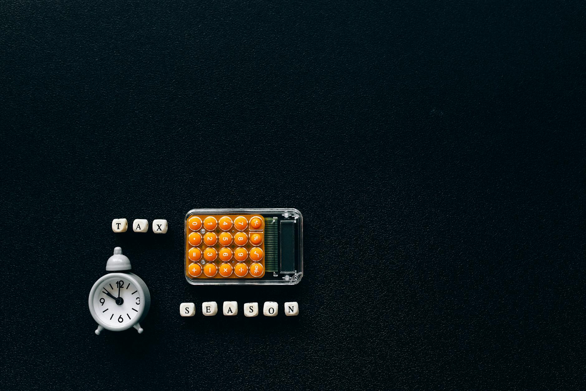 Flat lay of a tax season theme with a clock and calculator on a dark background. - workplace dating policy