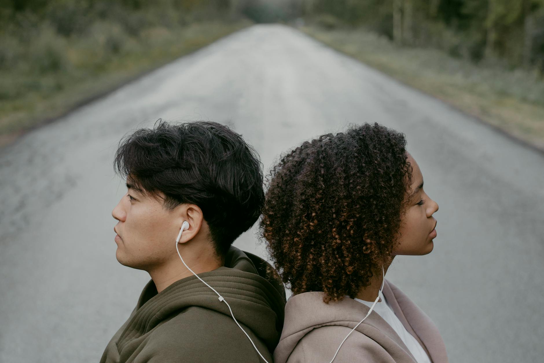 A couple sits back to back, sharing headphones, on an open road. Diverse unity in music. - active listening couples
