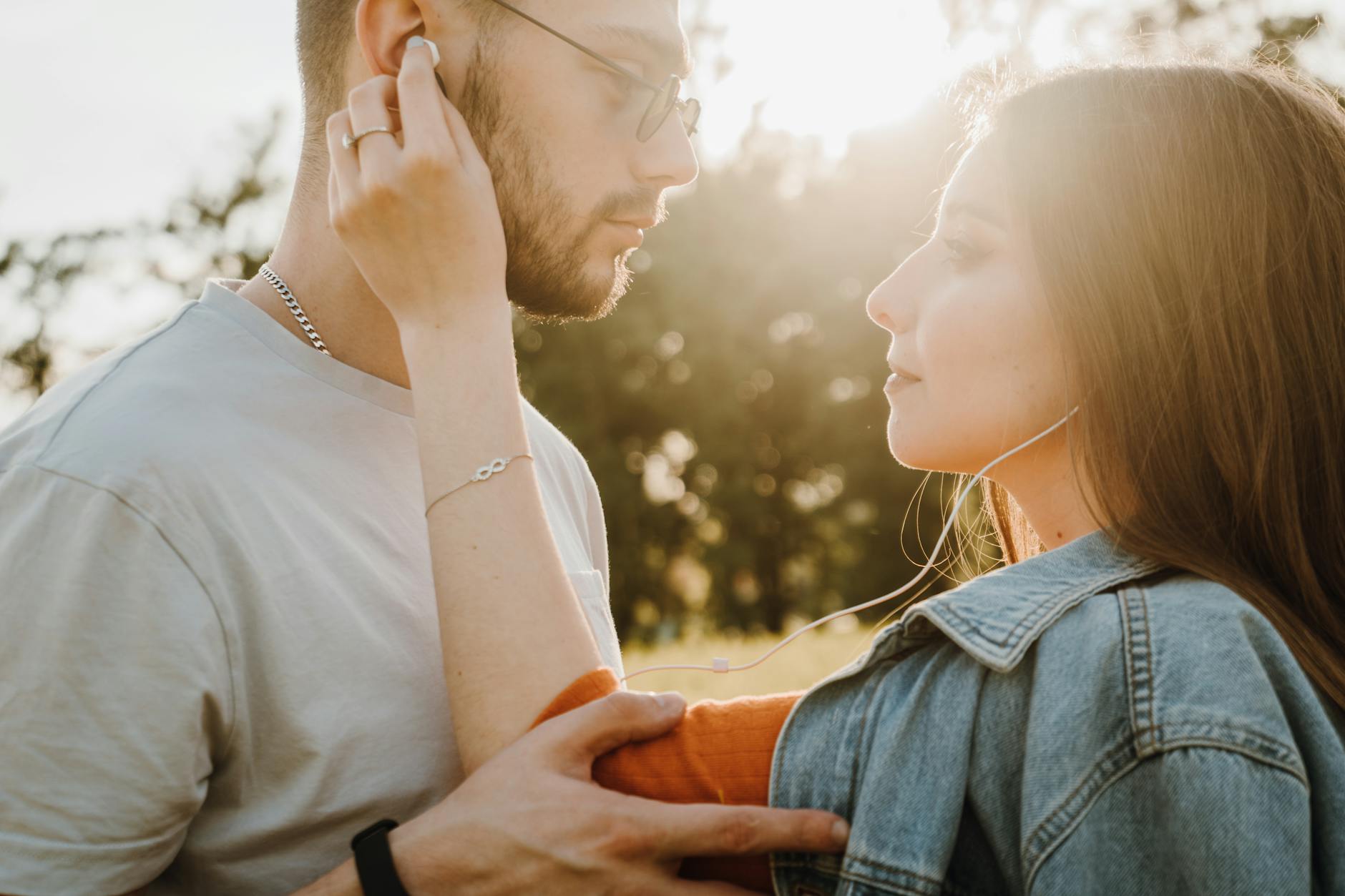 A loving couple shares earphones and a tender moment in a sunny outdoor setting. - active listening couples