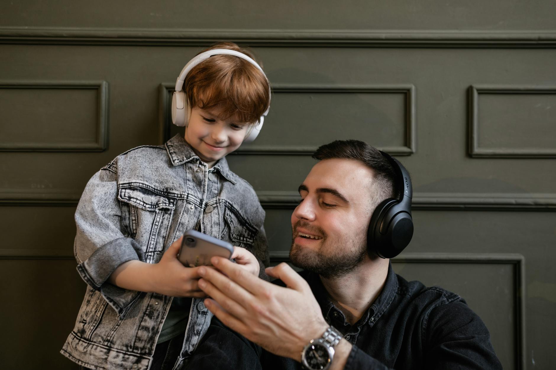 Father and son sharing joyful music moments indoors with headphones and a smartphone. - active listening kids