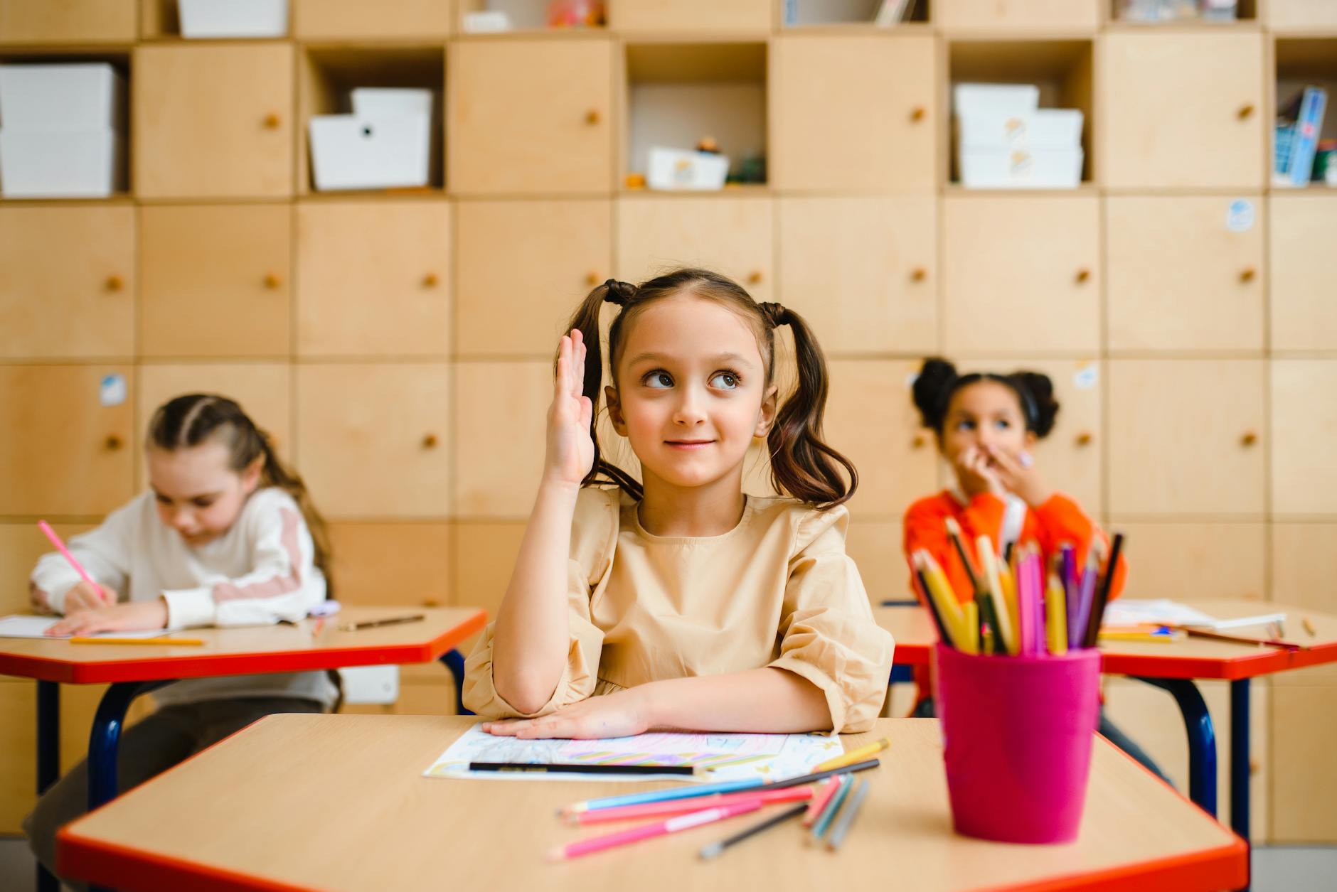 Young girl raises her hand during a lesson in a bright classroom. - active listening kids