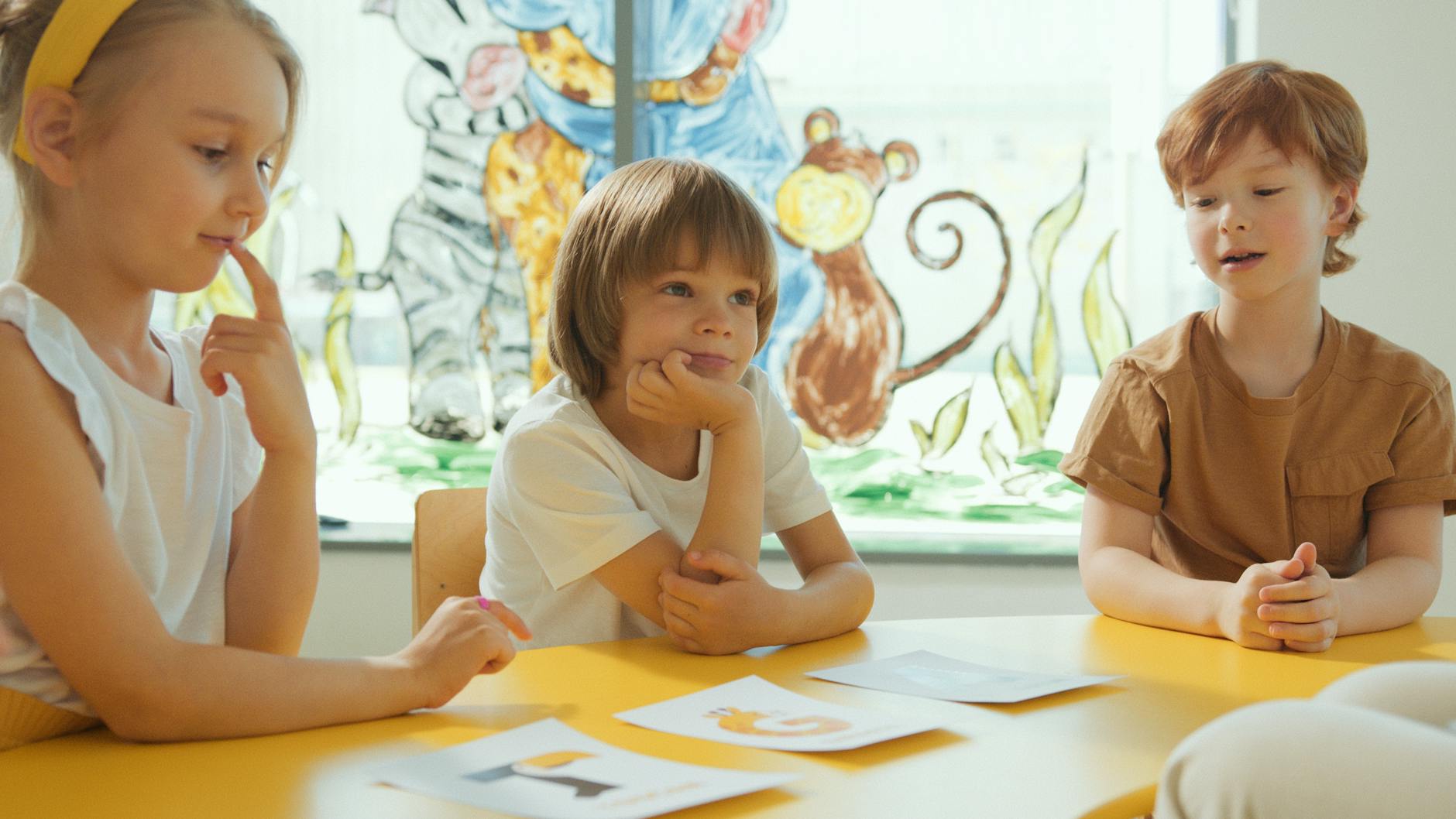 Three children sitting at a yellow table in a classroom, engaging in a learning activity. - active listening kids