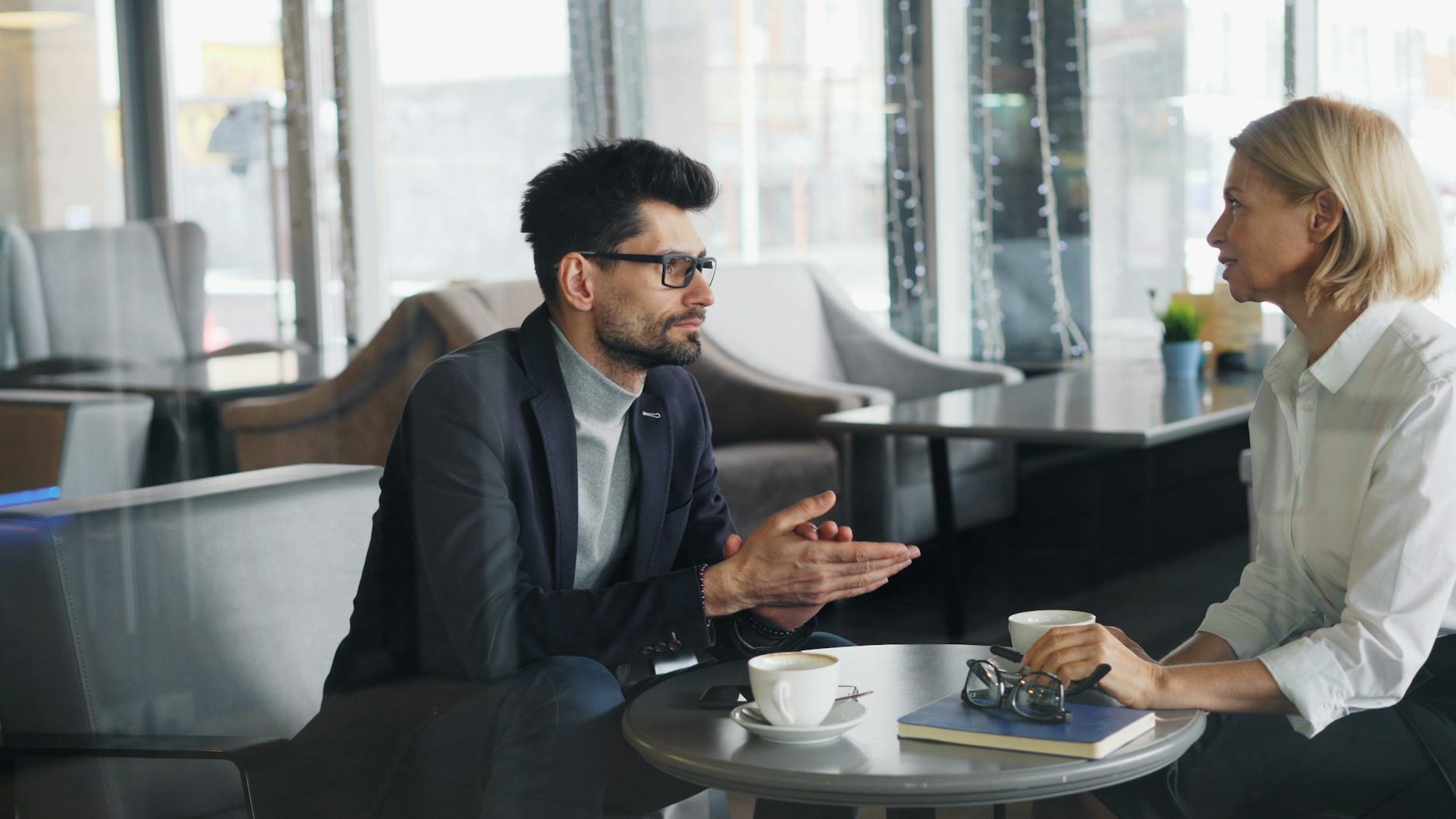 Professional man and woman discussing business topics over coffee in a contemporary cafe. - active listening partner