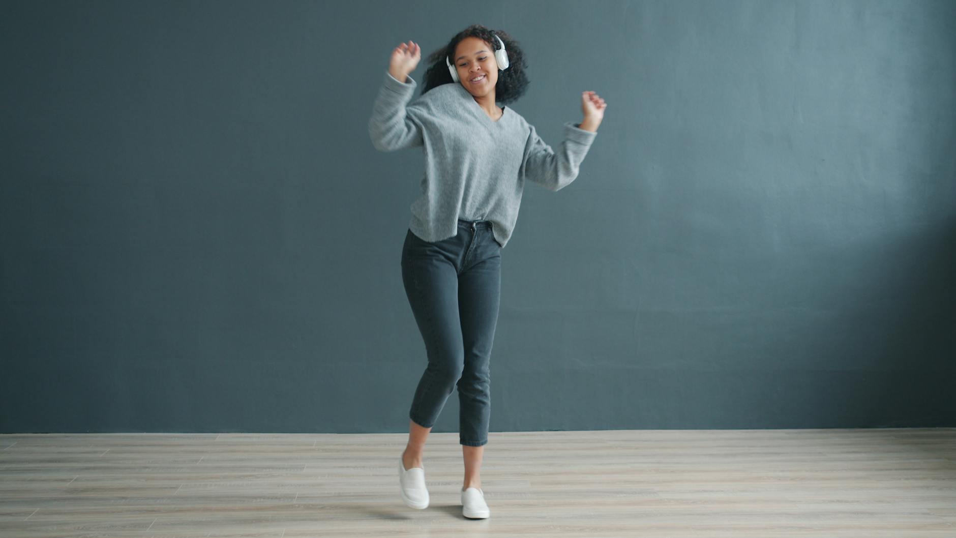 Happy young woman dancing with headphones on, enjoying music in a modern room. - active listening partner