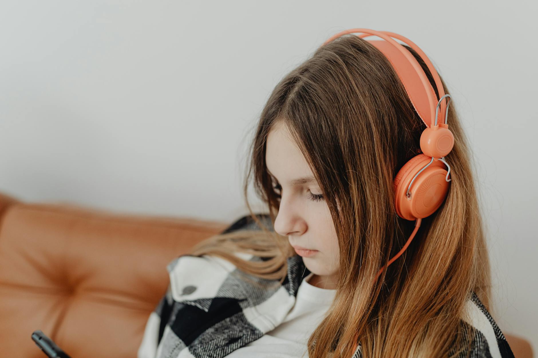 A young woman with brown hair wearing orange headphones, deeply engaged in listening to music. - active listening teen