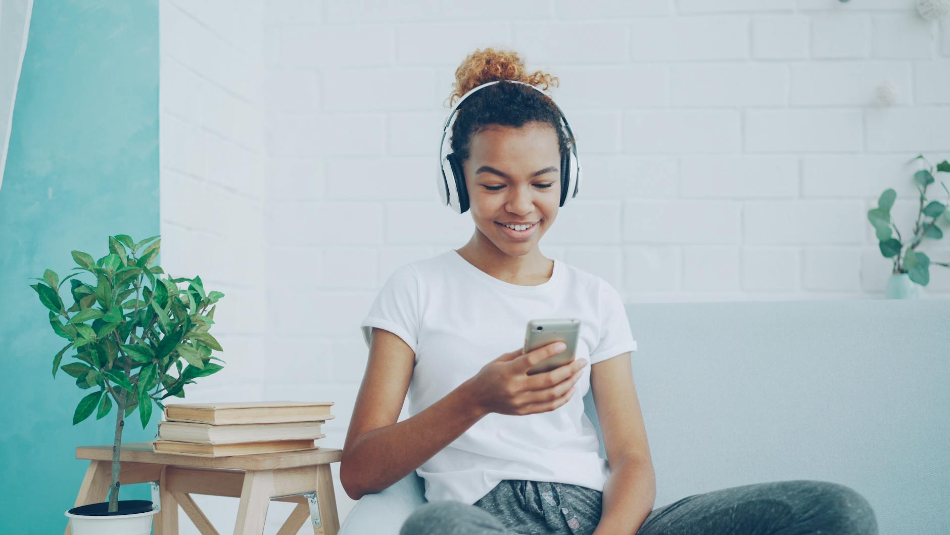 Smiling teen girl enjoying music on headphones while texting on smartphone at home. - active listening teen