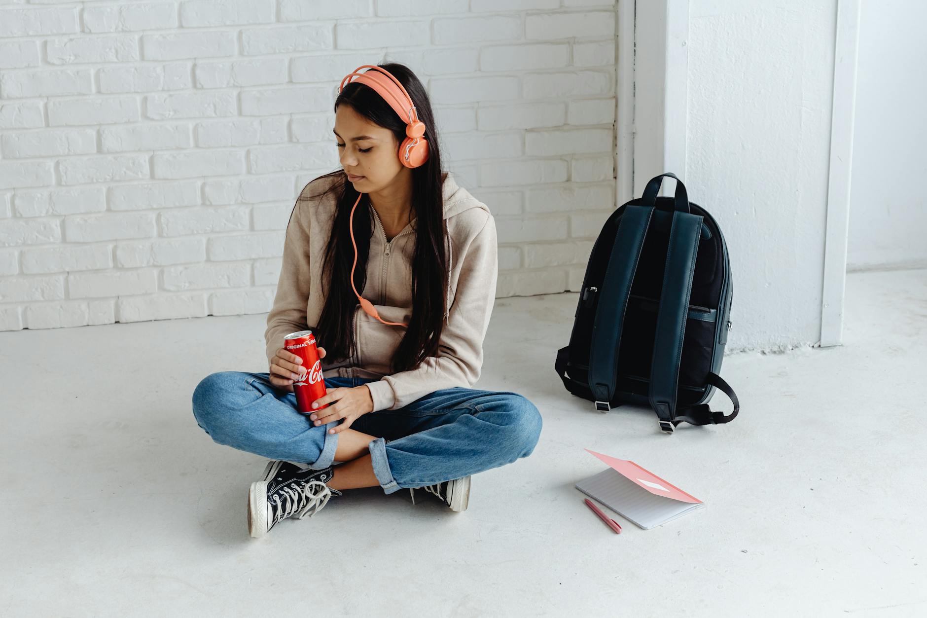 Teen girl with headphones, sitting in corridor, enjoying a drink in a relaxed atmosphere. - active listening teens