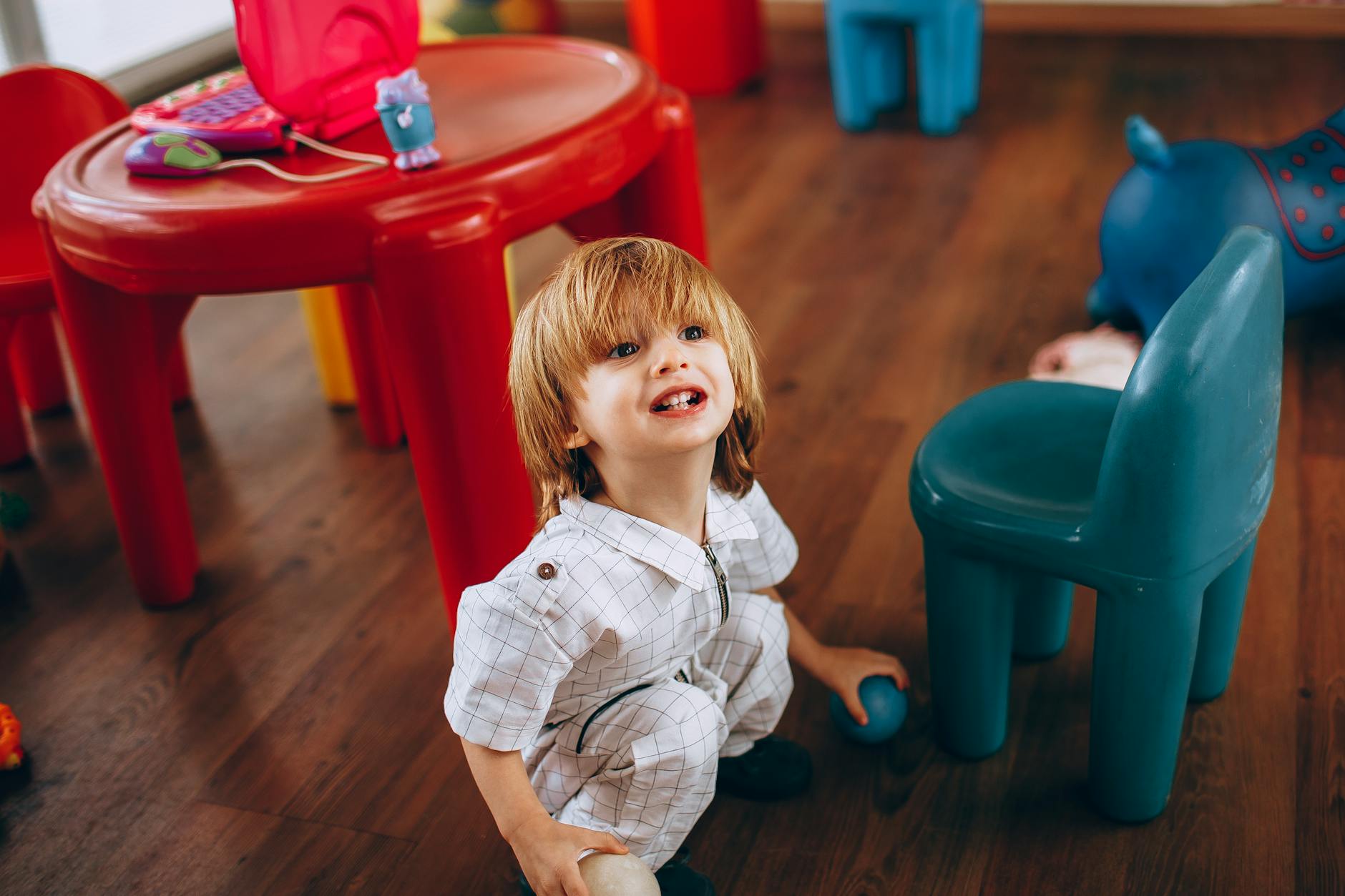 Young child in white outfit enjoying playtime in a vibrant indoor playroom with colorful toys. - active listening toddlers