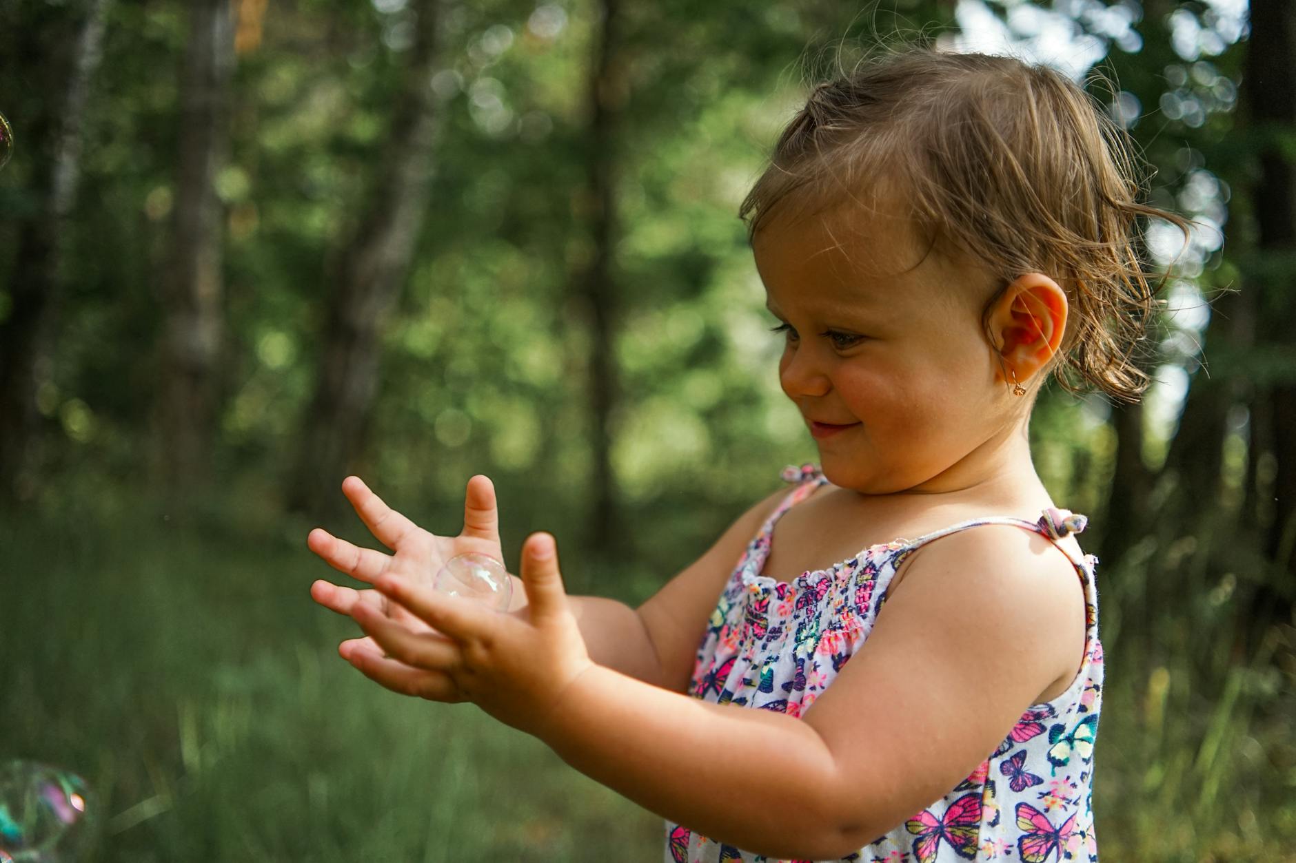 A smiling toddler plays with soap bubbles in a sunny forest setting, capturing the essence of childhood joy. - active listening toddlers