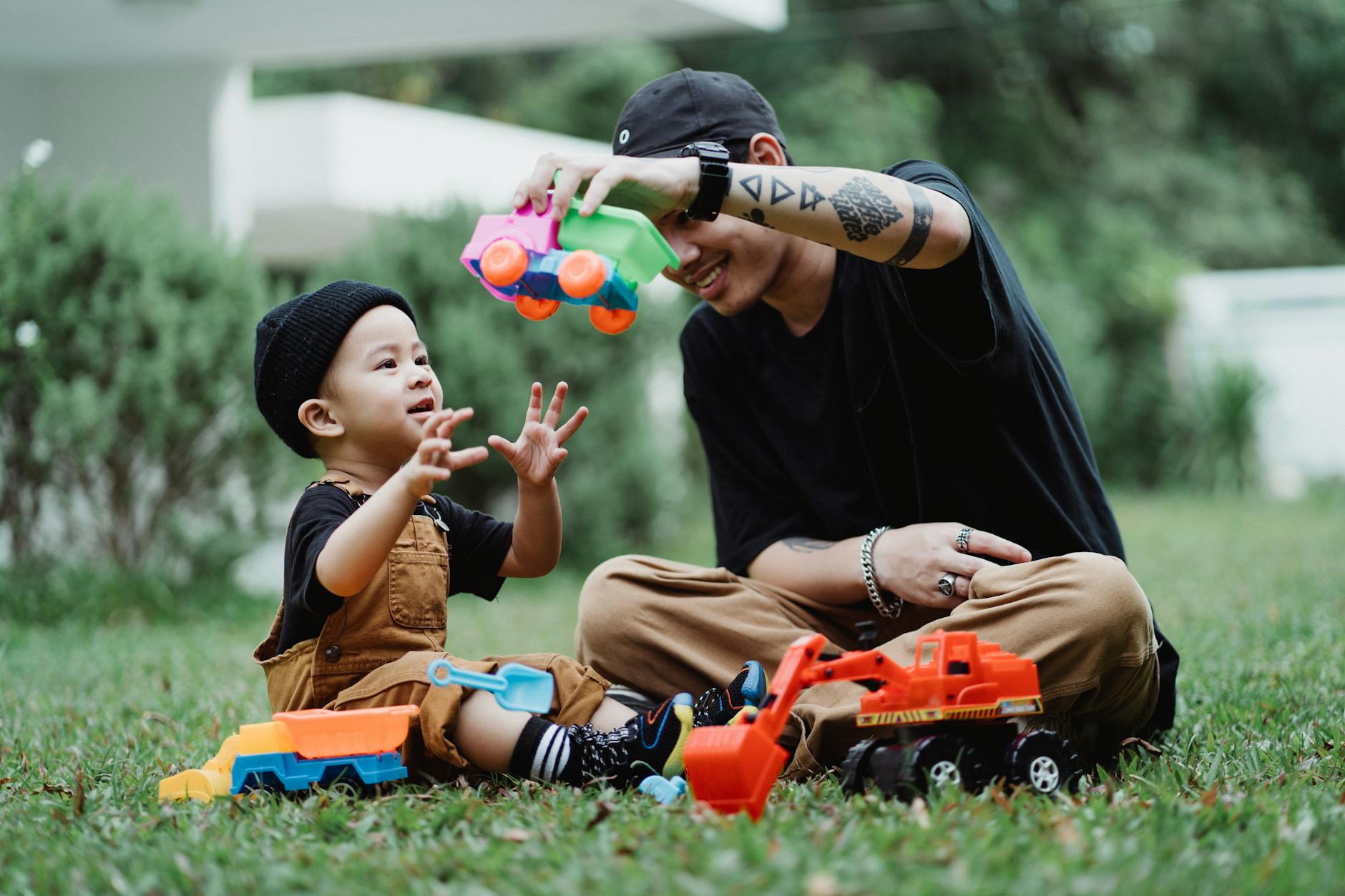 Young father and son enjoying playtime with toy cars in a sunny garden setting. - active listening toddlers