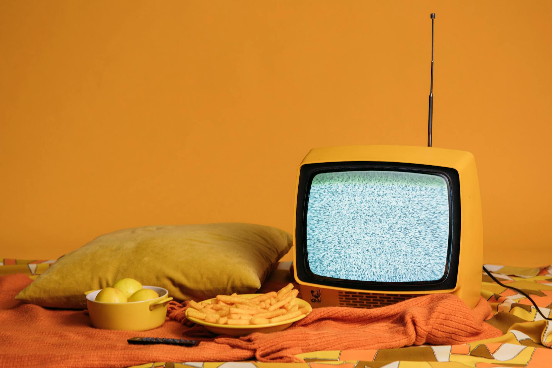 A vintage yellow TV with static, surrounded by fries, apples, and a cozy pillow setup. - anger management tv shows