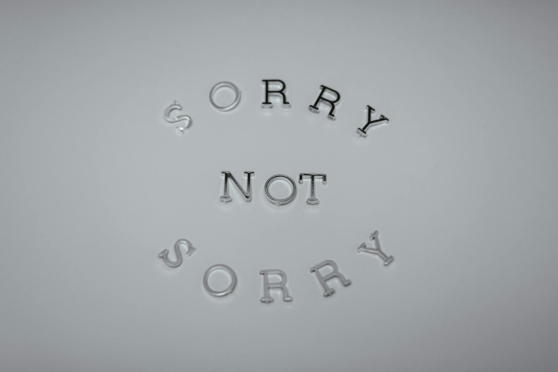 Minimalist design featuring the phrase 'Sorry Not Sorry' arranged in a circular pattern on a white background. - what does apologize mean