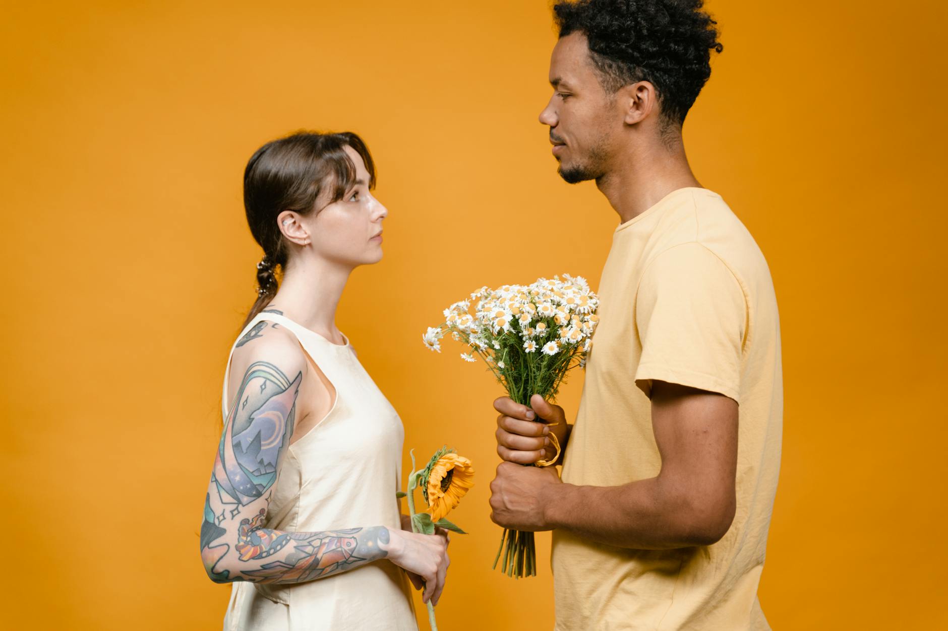 Two adults facing each other, holding flowers on a vibrant yellow background. - what does apologize mean