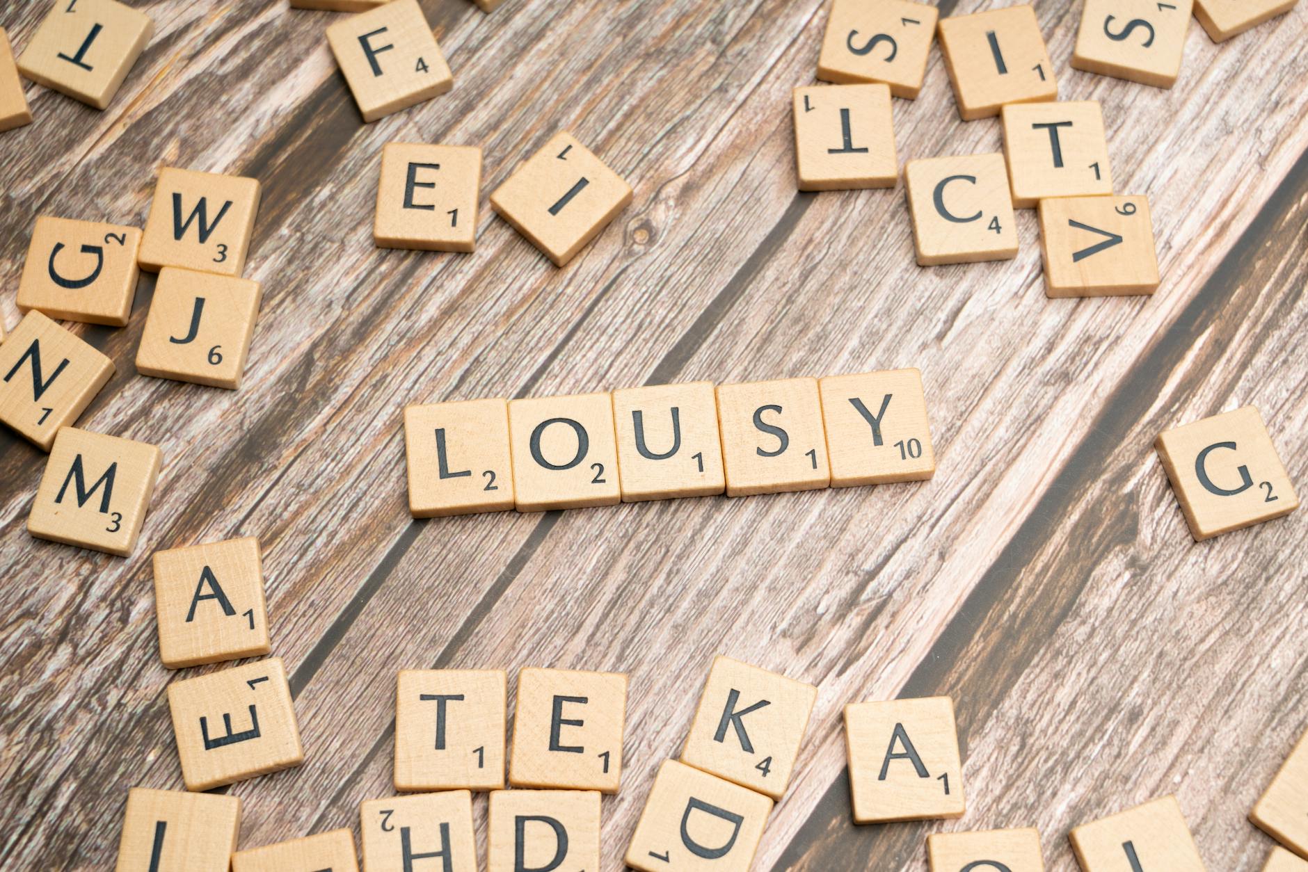 Scrabble tiles on a wooden table forming the word 'lousy' with scattered tiles around. - bad apology examples