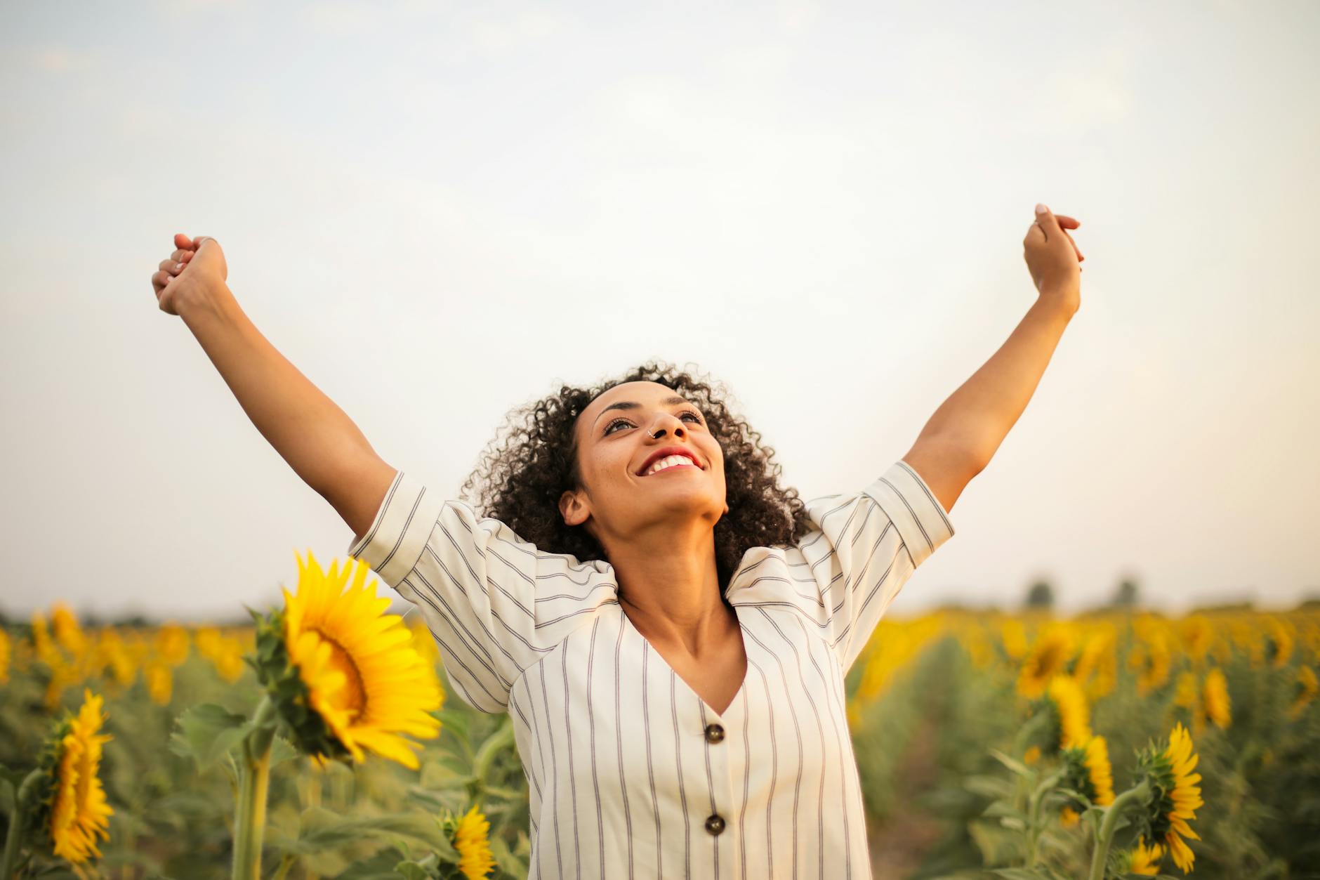 Joyful woman with arms raised in a sunflower field, embracing freedom and happiness. - boost mood naturally