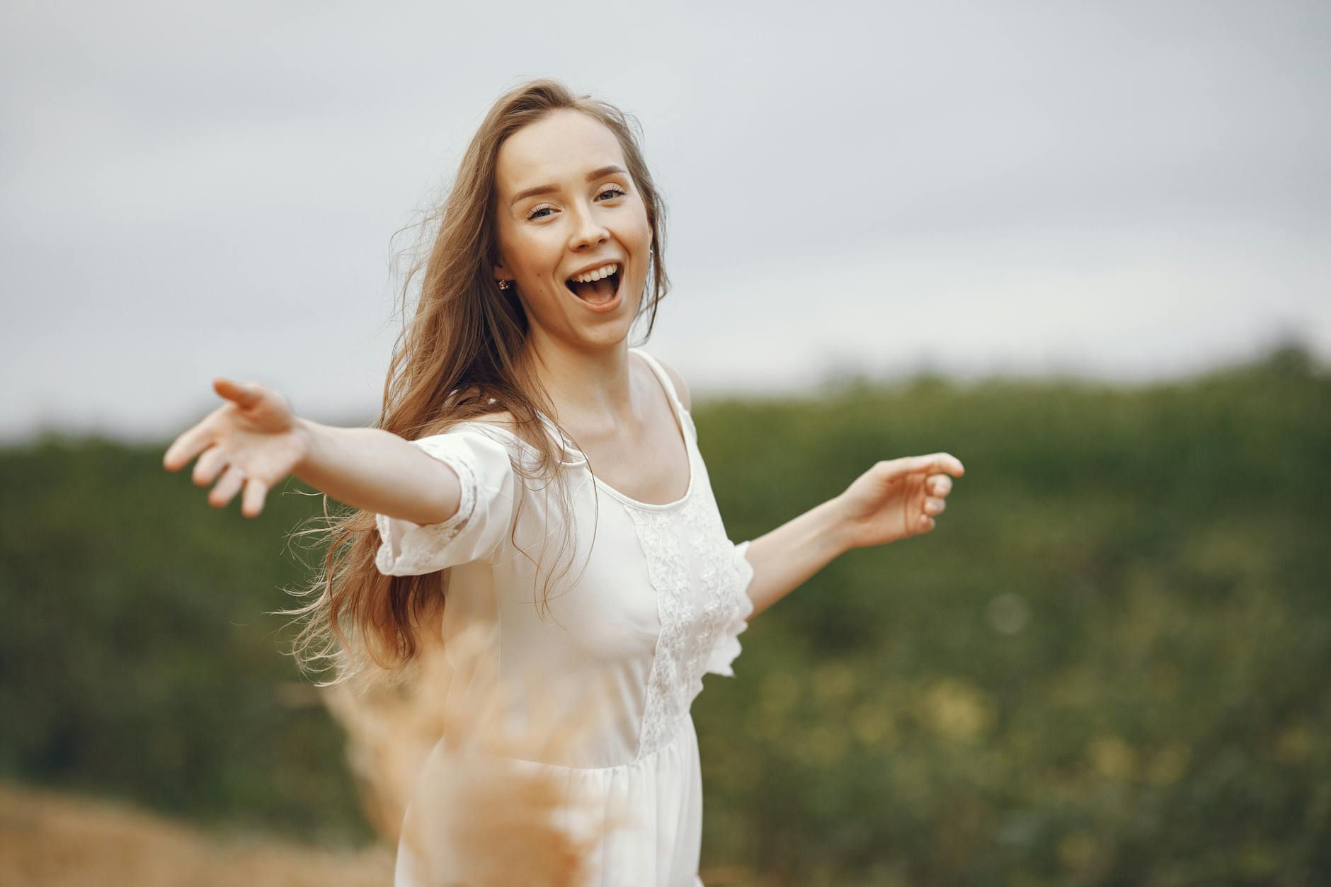 Smiling woman in a white dress enjoying nature with open arms. - boost mood naturally