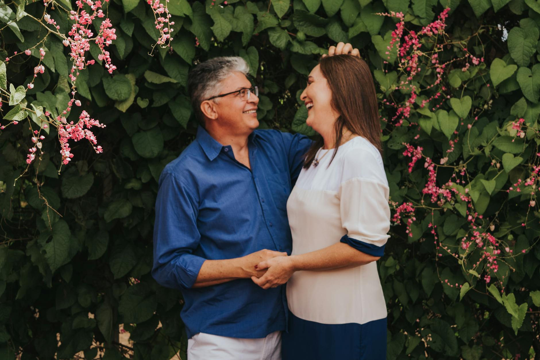 Senior couple embracing with joy surrounded by green foliage and pink flowers, capturing a moment of love and happiness. - build trust couples