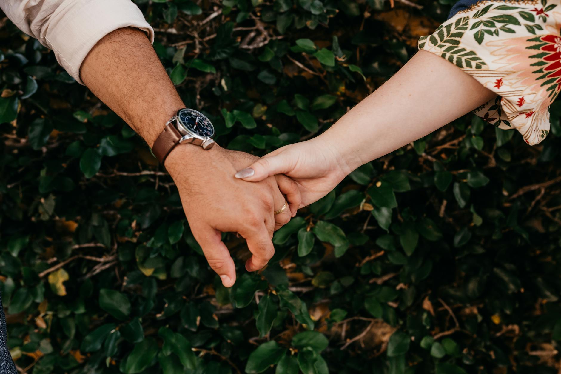 A close-up of a couple holding hands against a leafy background, symbolizing connection. - build trust couples