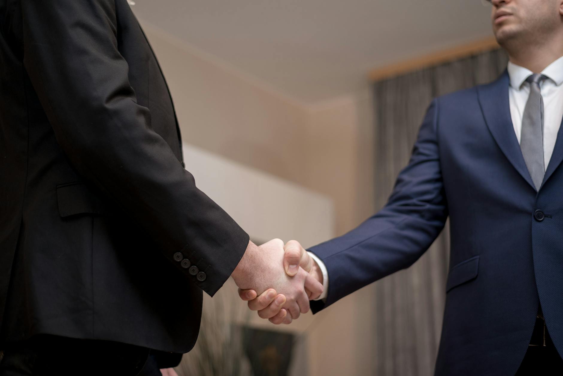 Two businessmen in suits shaking hands, emphasizing trust and partnership indoors. - build trust partner