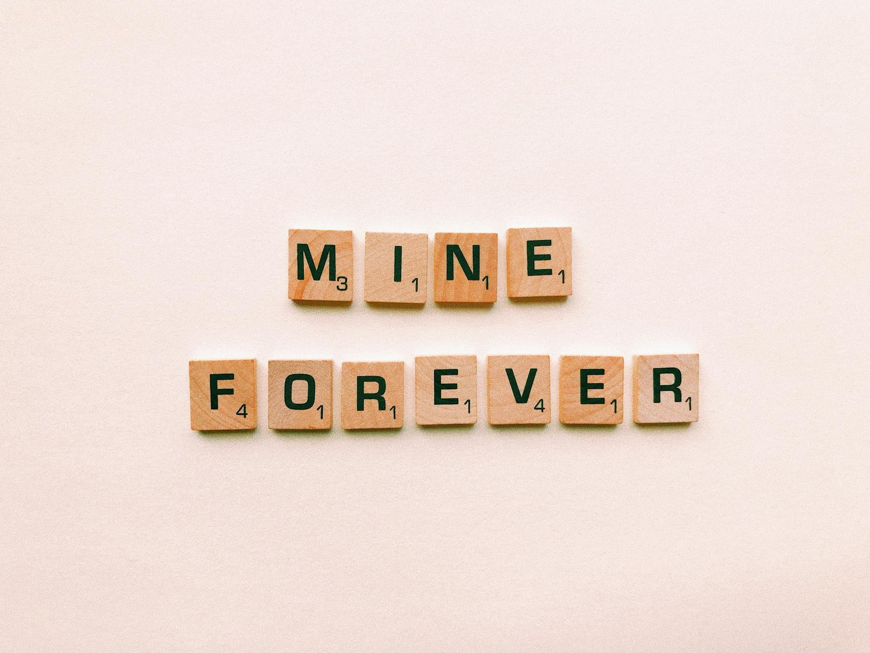 Scrabble tiles spelling 'Mine Forever' on a pink background, symbolizing romance. - casual to committed relationship