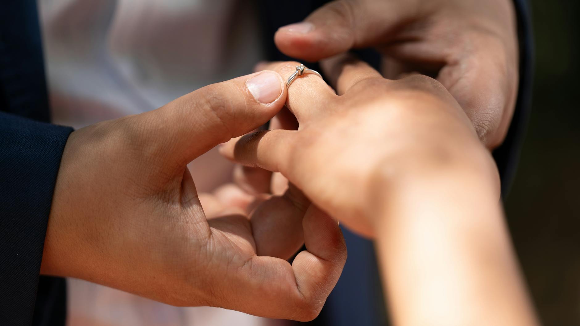 Close-up of an engagement ring being placed on a woman's hand in natural lighting. - casual to committed relationship