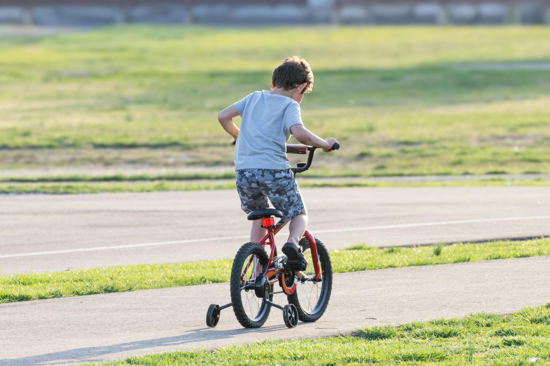 Young boy riding a bicycle with training wheels in a park on a sunny day. - child development milestones
