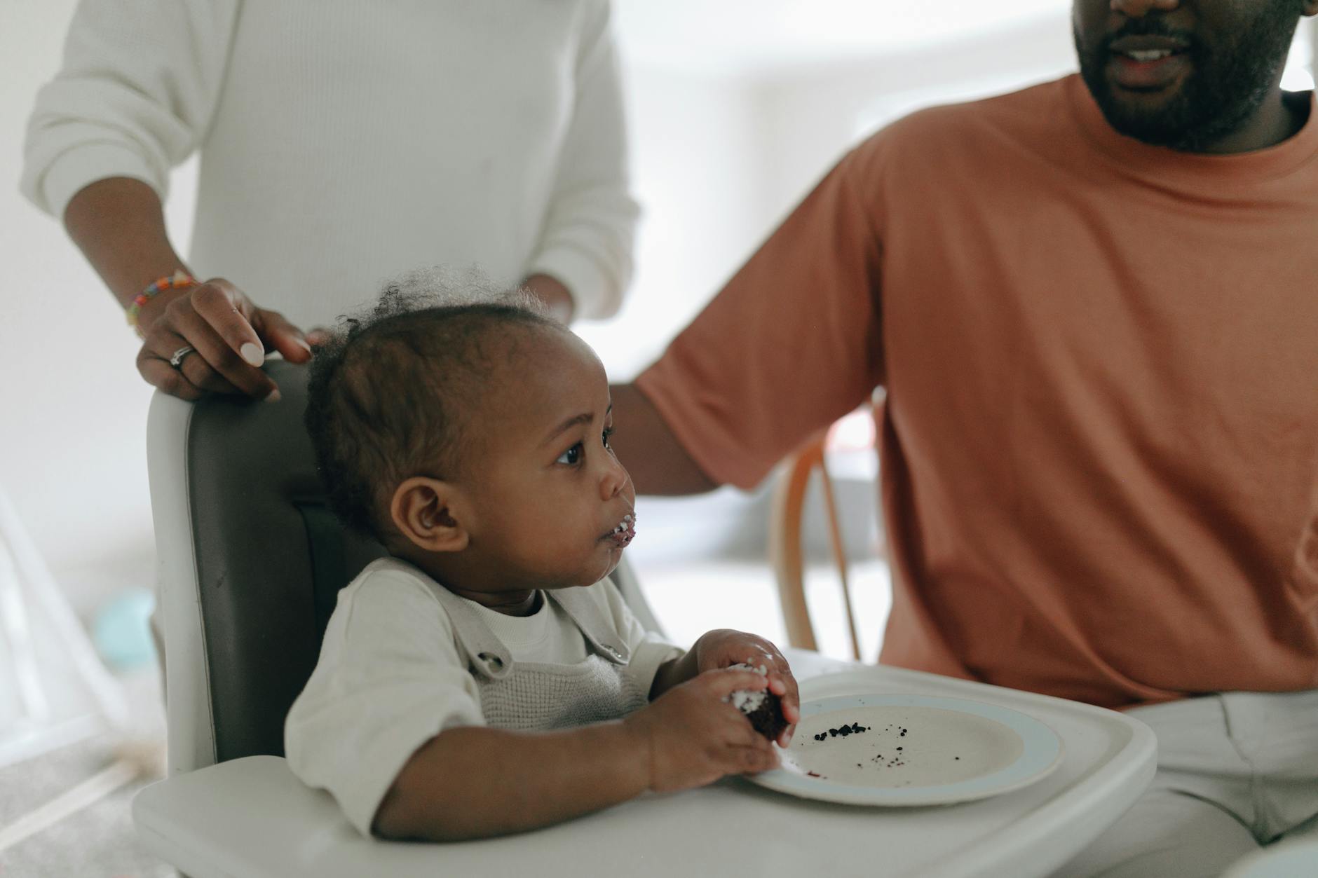 Black baby enjoying cake with family during first birthday celebration. - child development milestones