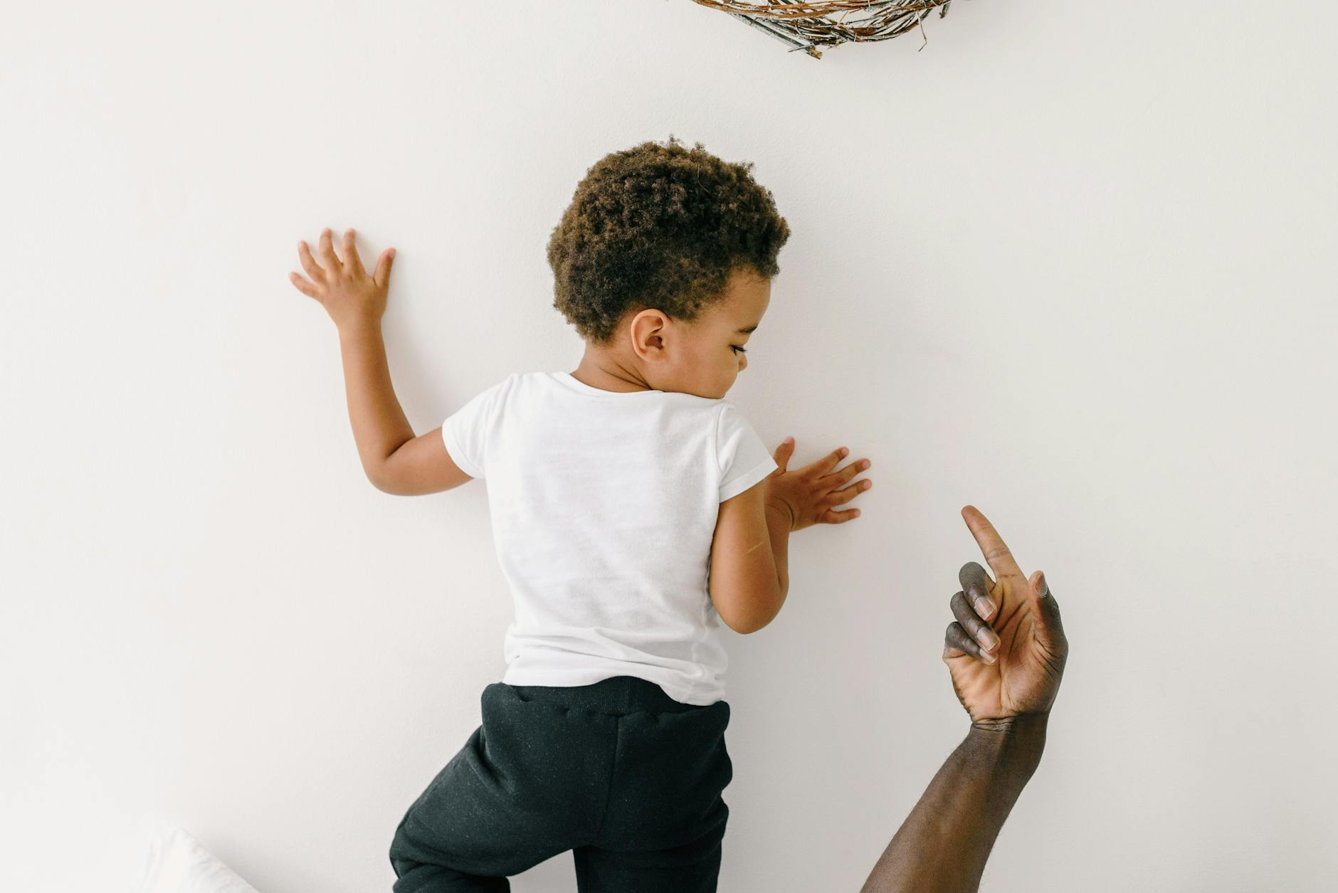 Young African American boy facing wall with adult guiding hand visible. - child growth spurt