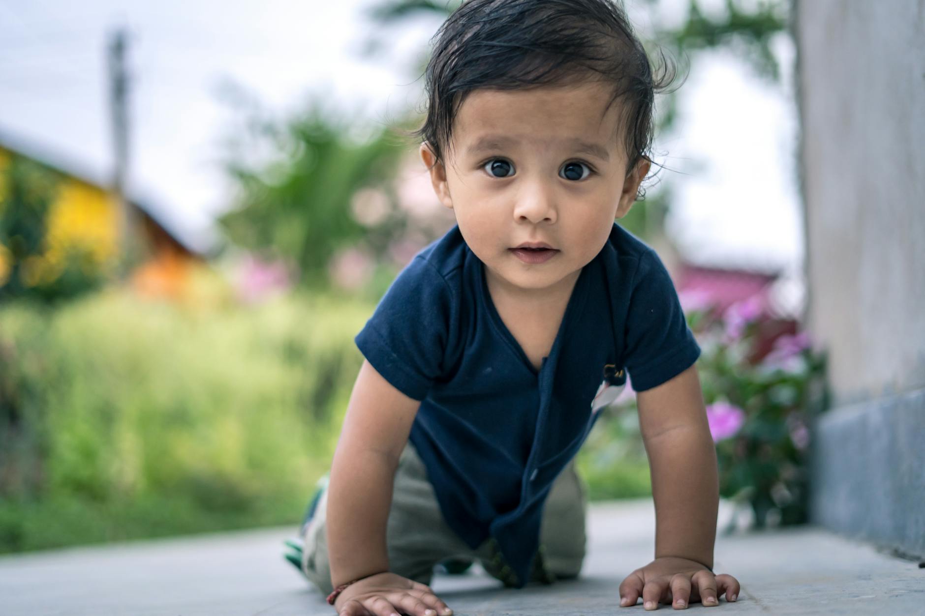 A cute baby in a blue shirt crawling outside on a sunny day, surrounded by greenery. - child growth spurt