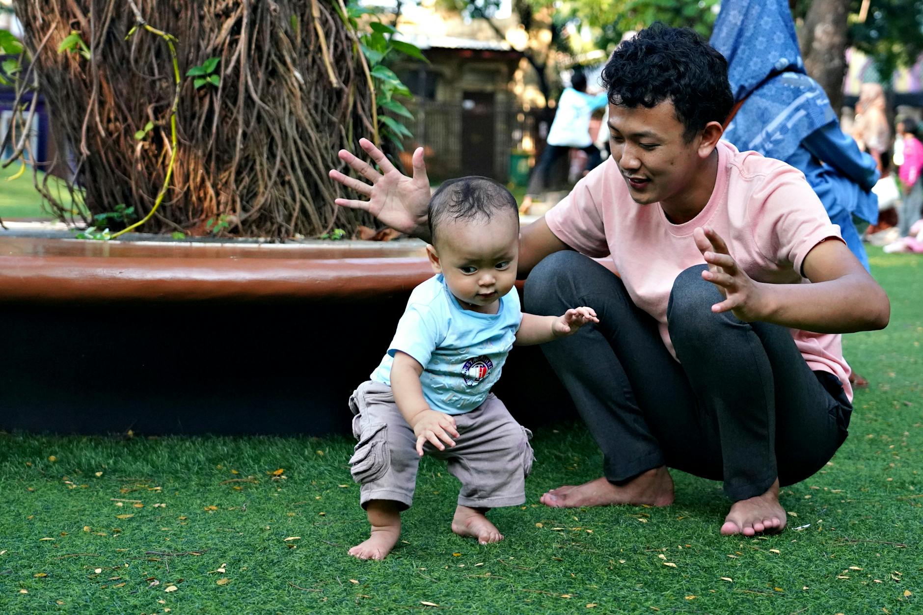 A father encourages his baby to take first steps on a sunny day in a park, barefoot on green grass. - child growth spurt