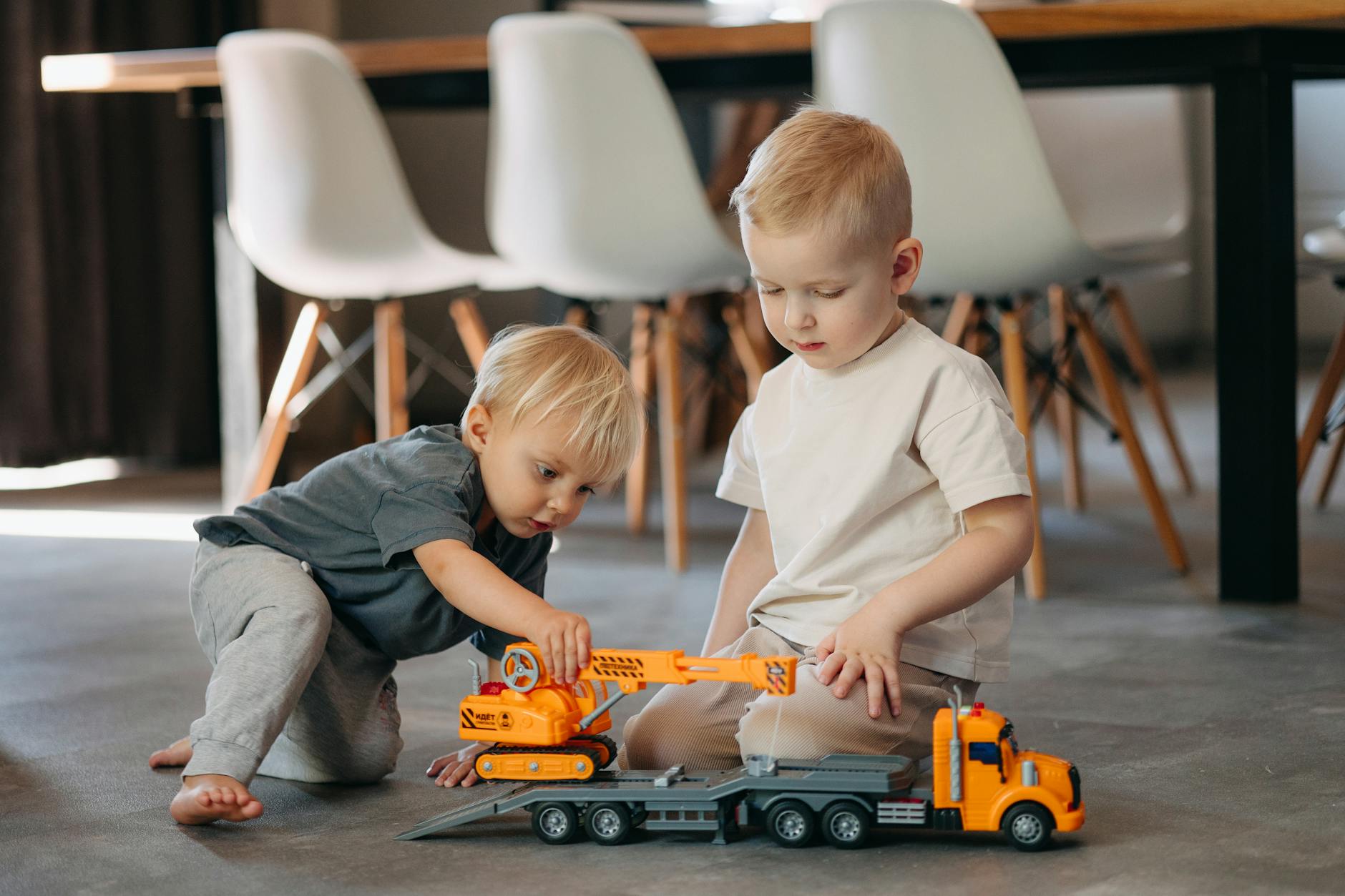 Two young boys playing with toy trucks on the floor in a modern indoor setting. - child social skills