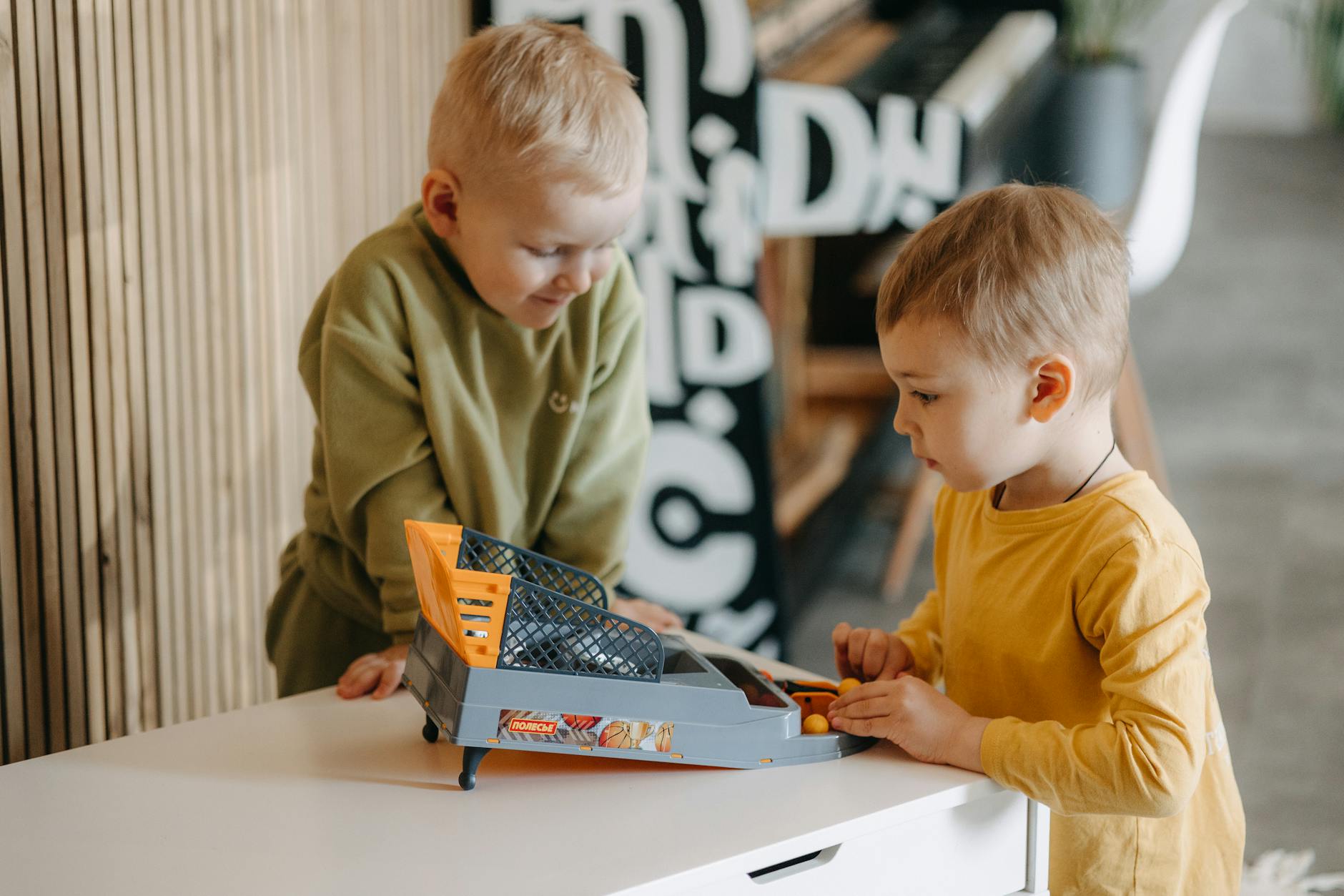 Two young boys enjoy playing with a tabletop basketball game indoors, capturing fun and creativity. - child social skills