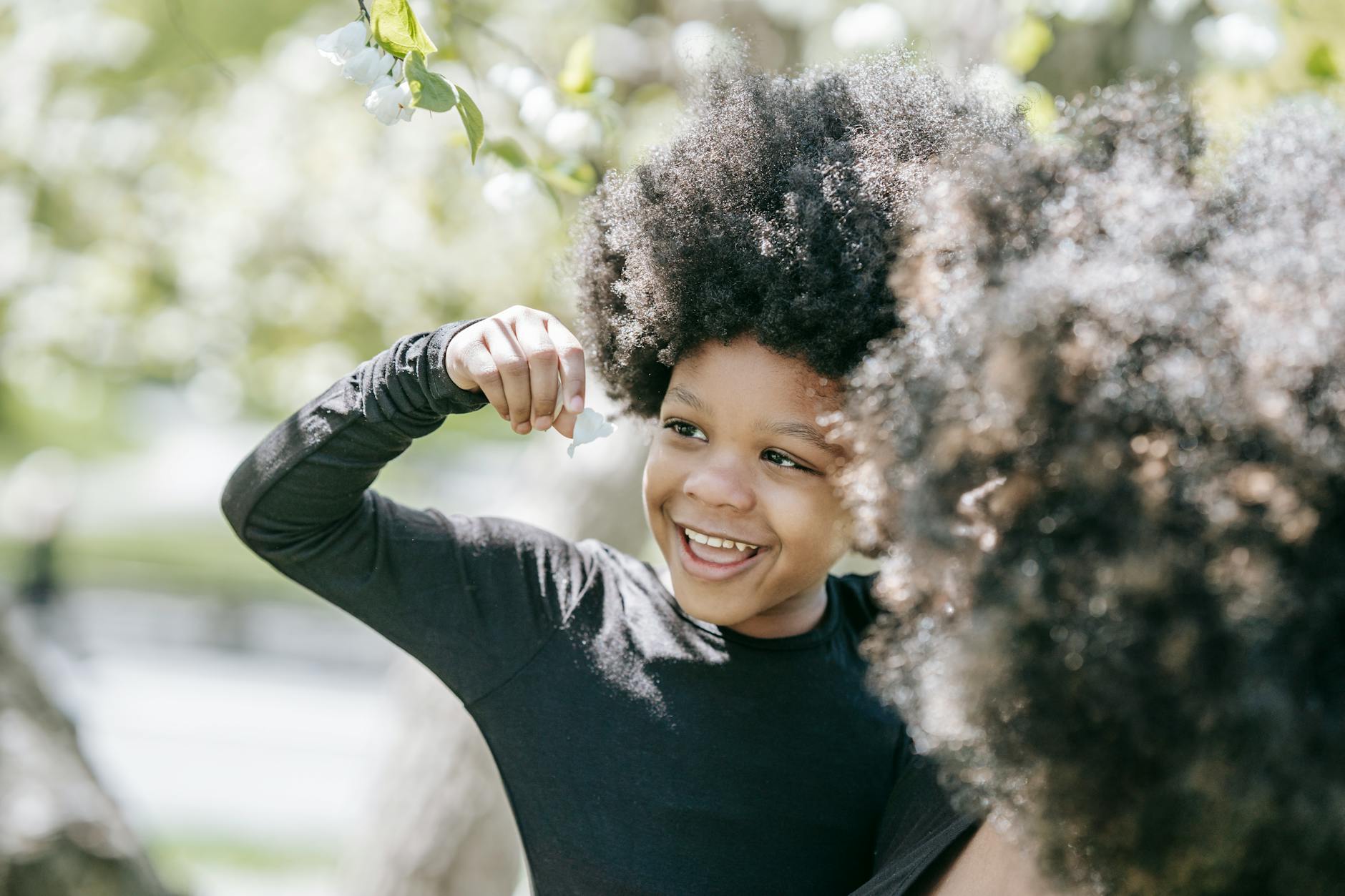 Happy child with curly hair enjoying springtime among blooming flowers. - child spring allergies