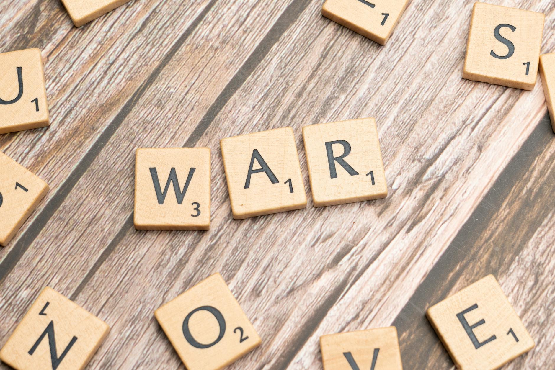 Close-up of wooden scrabble tiles spelling 'WAR' on a wooden background. - conflict meaning