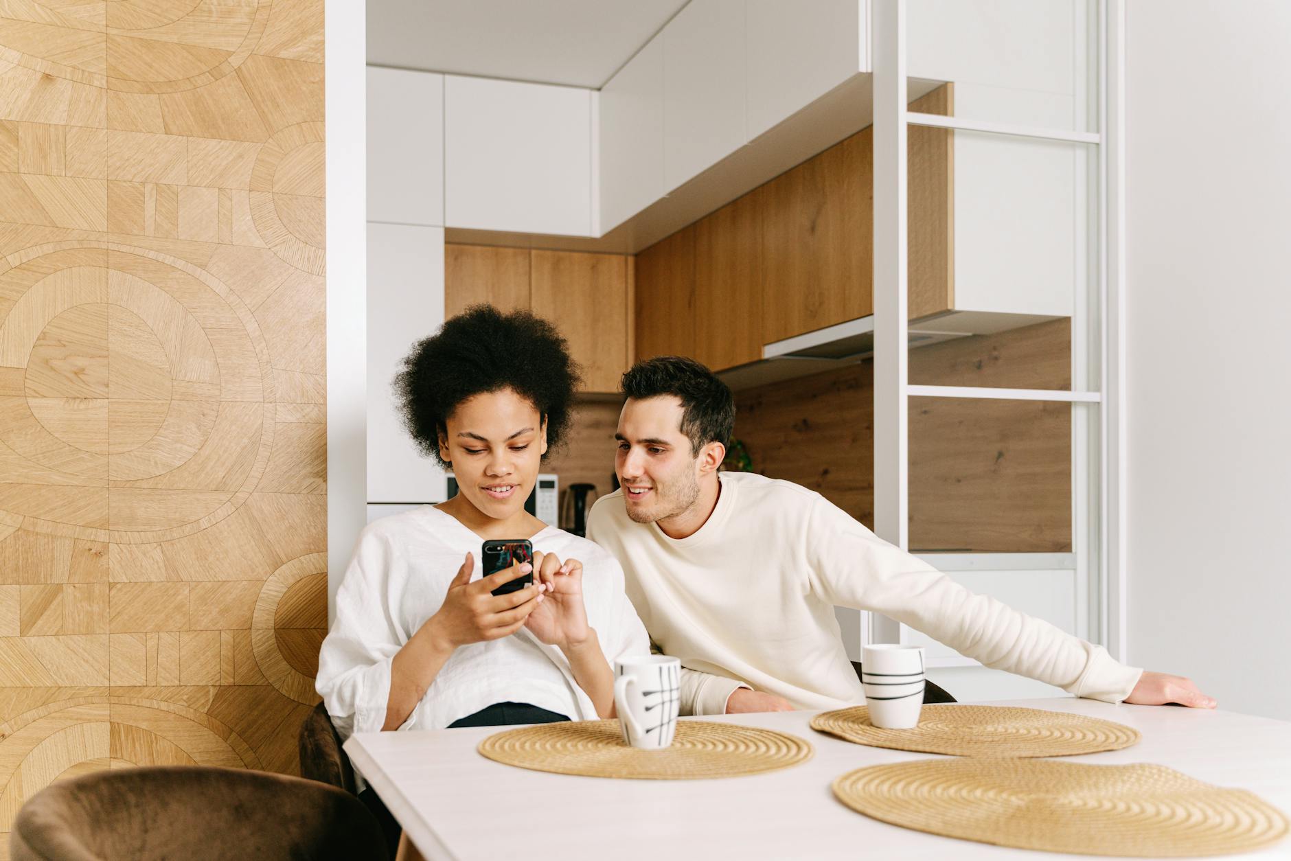 Interracial couple using a cellphone in a modern kitchen, expressing connection and technology. - couple communication needs