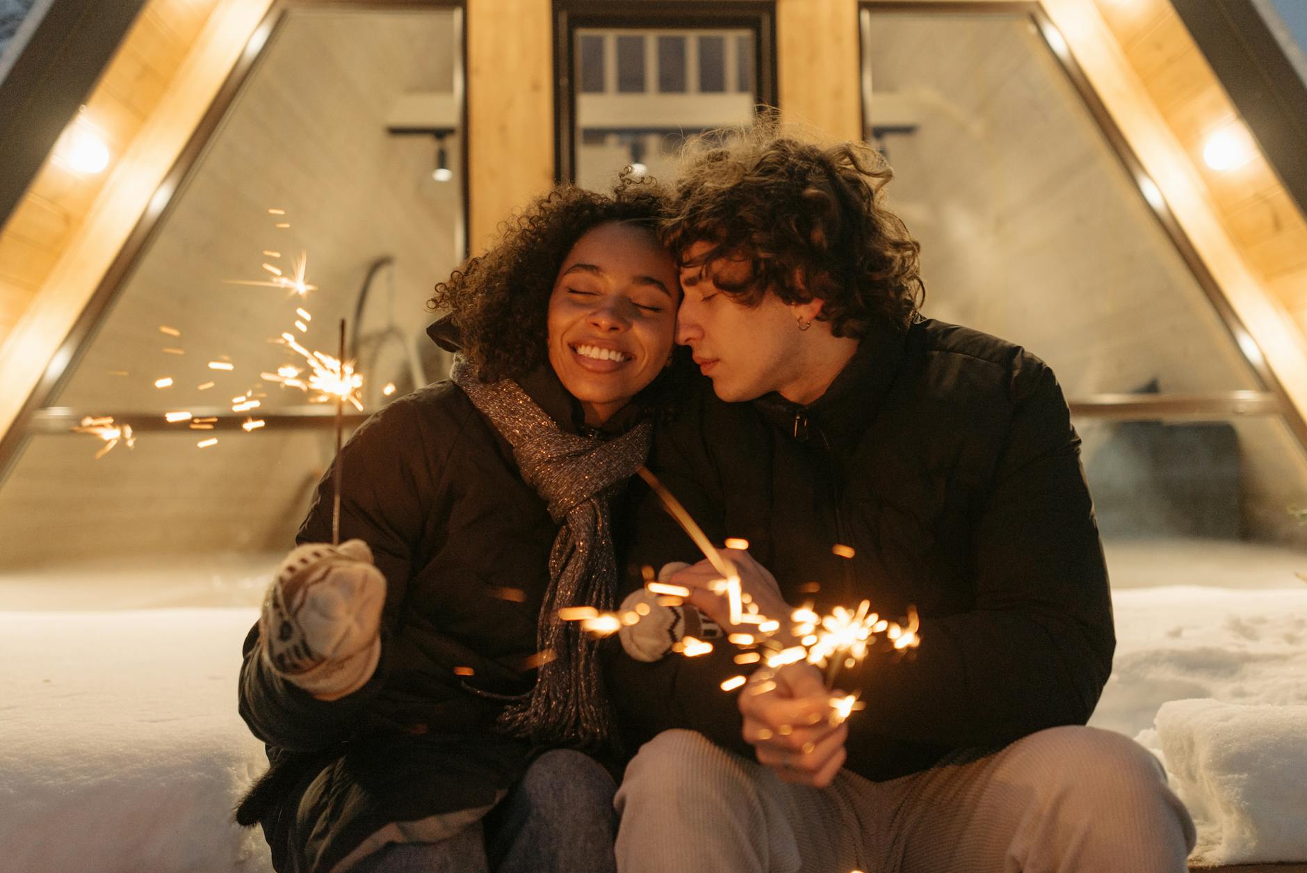 A joyful couple enjoying sparklers outside a cozy cabin in winter attire. - couple resolutions
