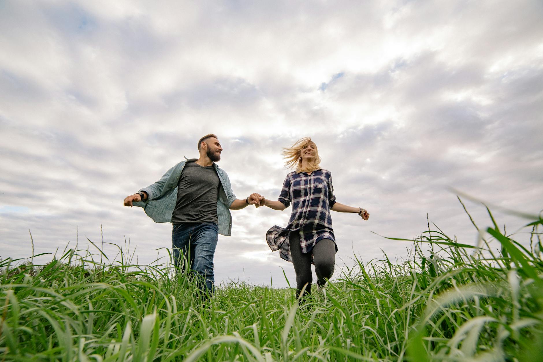 Happy couple holding hands and running in green field under cloudy sky, enjoying nature and freedom. - couple spring activities