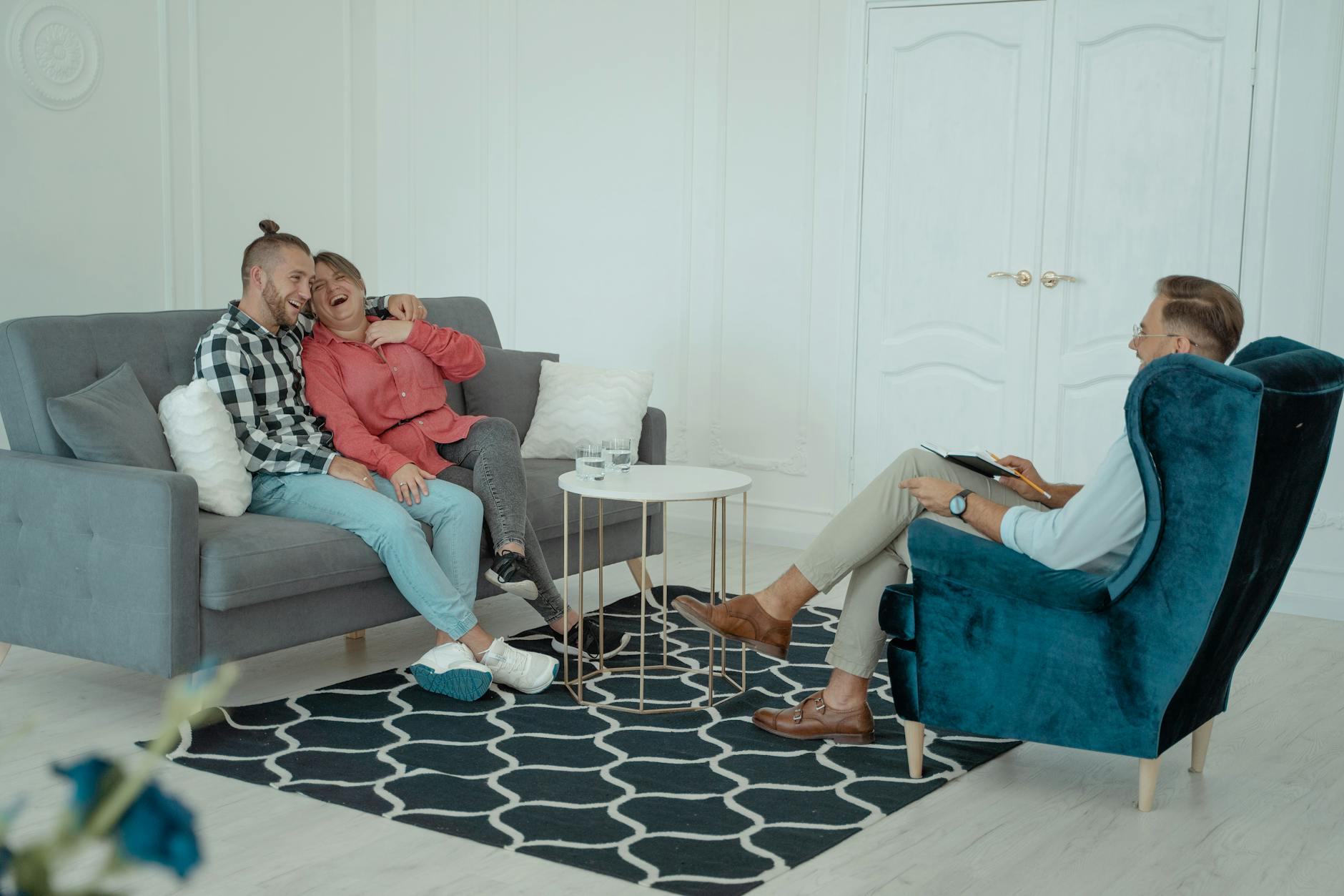 A happy couple enjoying a light moment in a therapy session with a therapist indoors. - couples therapy benefits