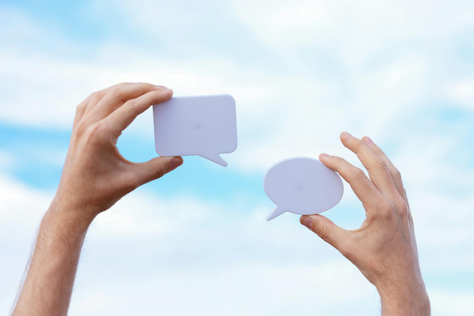 Close-up of hands holding speech bubbles, symbolizing communication and dialogue against a blue sky. - declutter communication